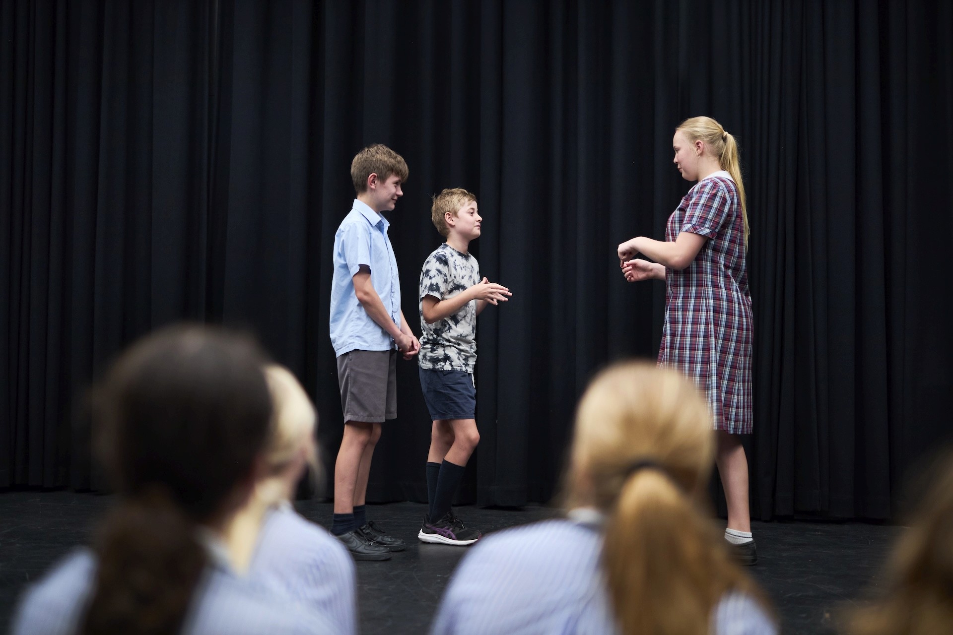 Older students stand spaced out in a dark-walled studio while a facilitator leads a movement activity.