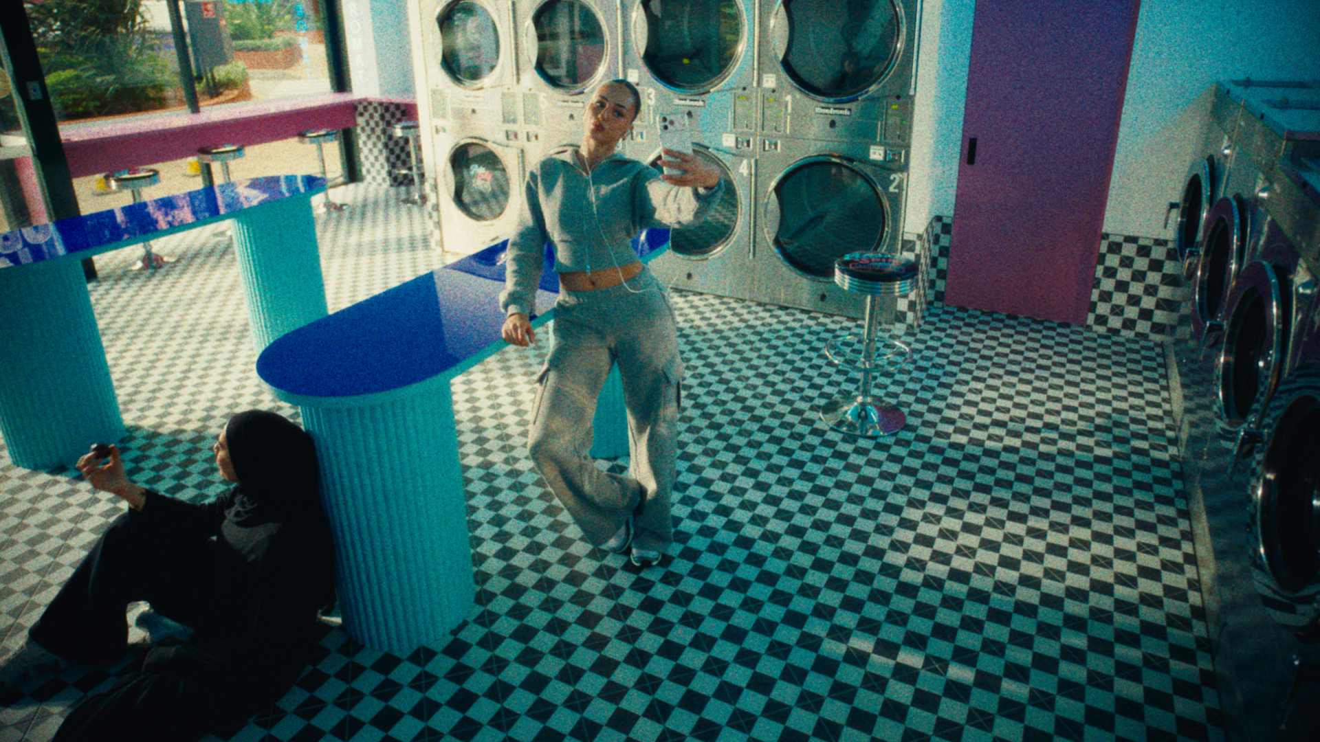 Two girls hang around in a pop art laundromat