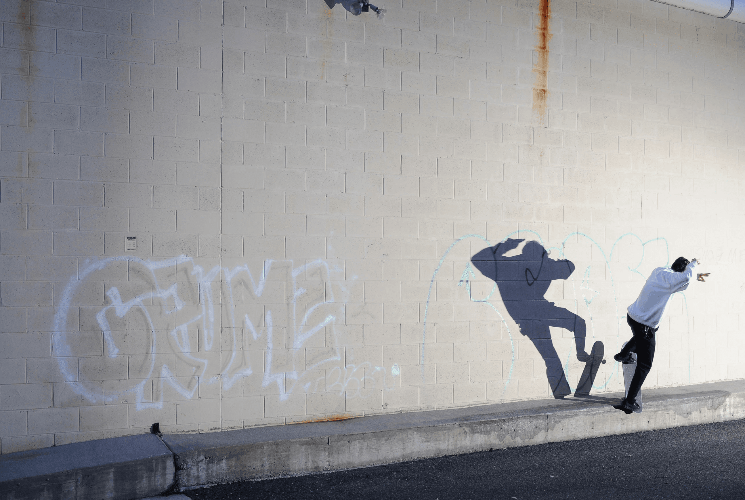 Digital photography of a skateboarder skating a ledge, lit agressively by a speed flash out of frame creating a bold enlarge shadow of the skater. 