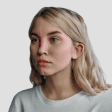 A young woman with blonde hair looking slightly to the side, wearing a white t-shirt against a plain, light grey background. A thin, vertical red line splits the center of her face.