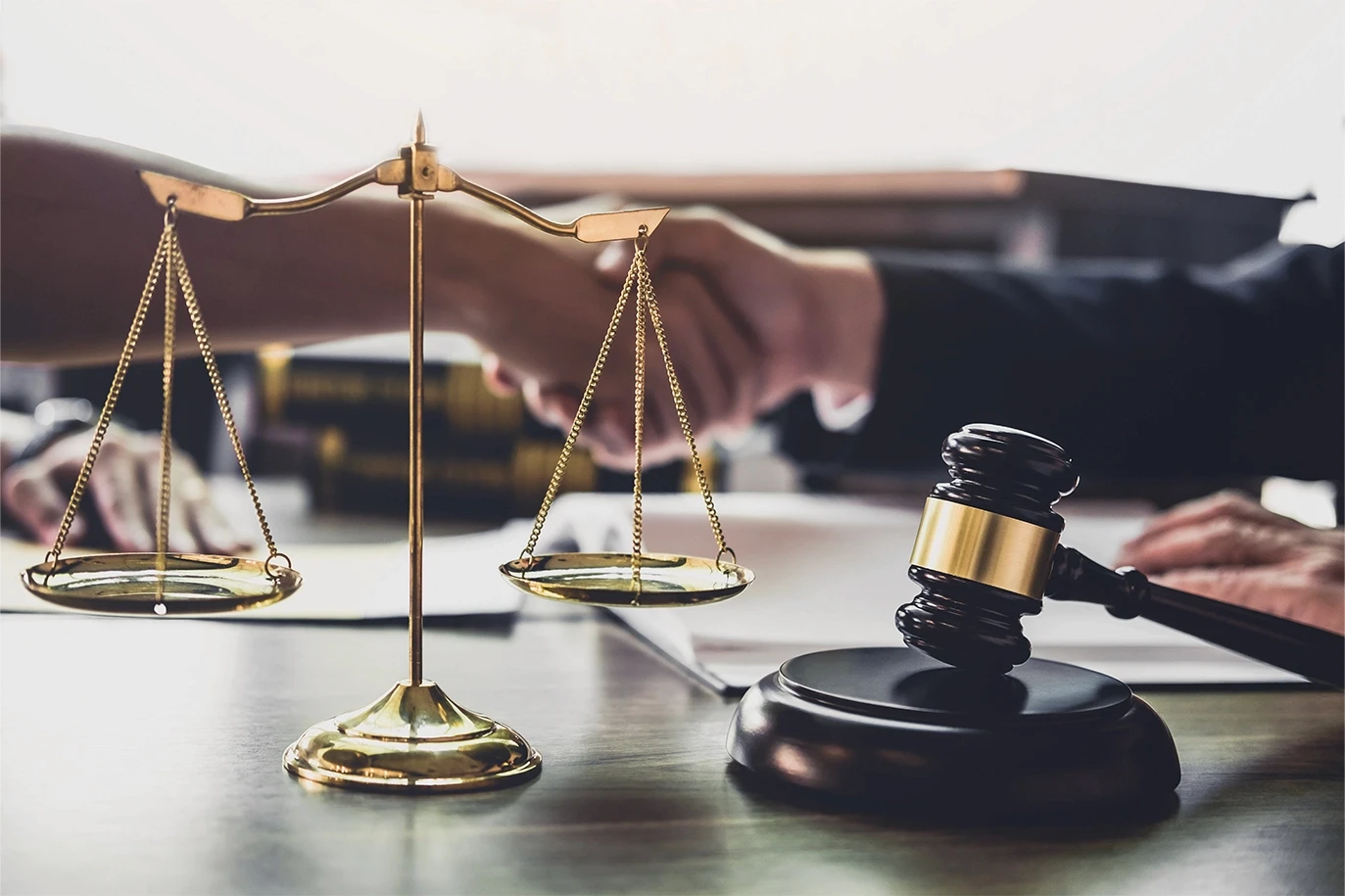 Scales of justice and gavel on an attorney’s desk with a handshake in the background, symbolizing representation and resolution in paralysis injury claims