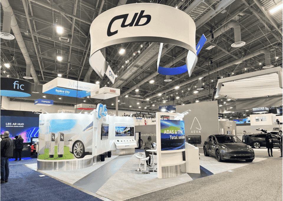 Large island industrial equipment demo booth with vehicle display and branded overhead sign for Las Vegas construction trade show exhibitors