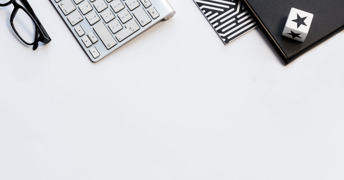 A stylish home office flat lay with a keyboard, glasses, and notebooks on a white backdrop.