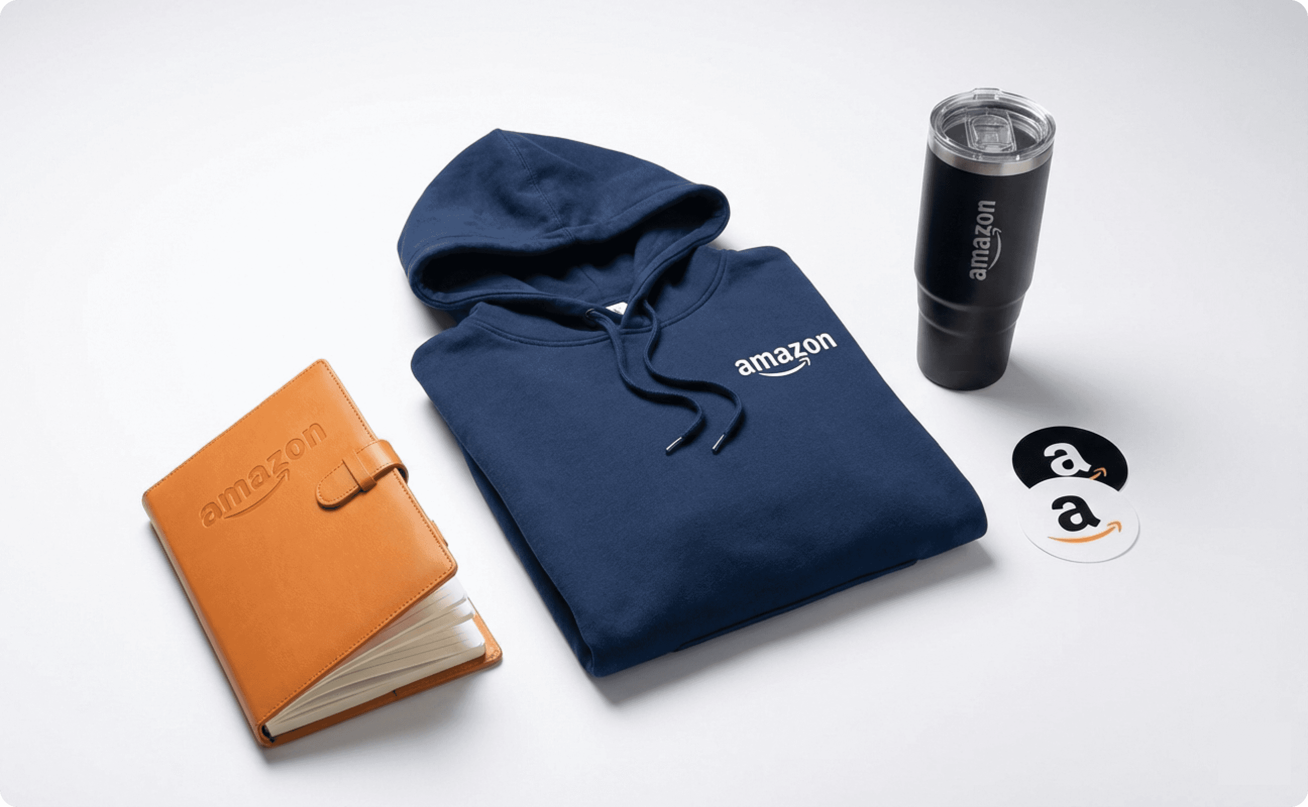 A notebook, a hoodie, a tumbler, and two stickers, all with Amazon logo.