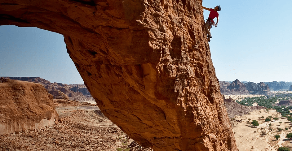 A climber pauses on a rock face to visualize their route on a unique rock formation in the country of Chad in northern Africa.