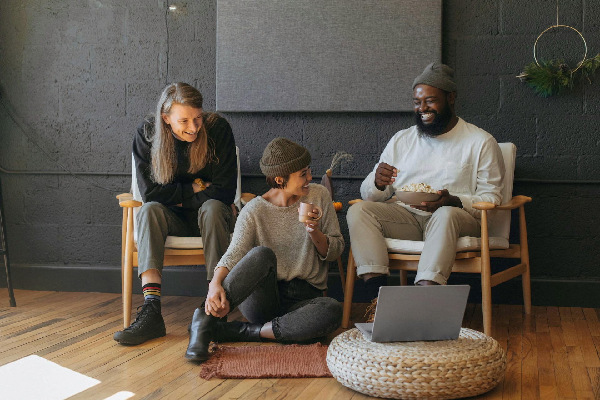 Three friends sitting and laughing while watching something on a laptop.