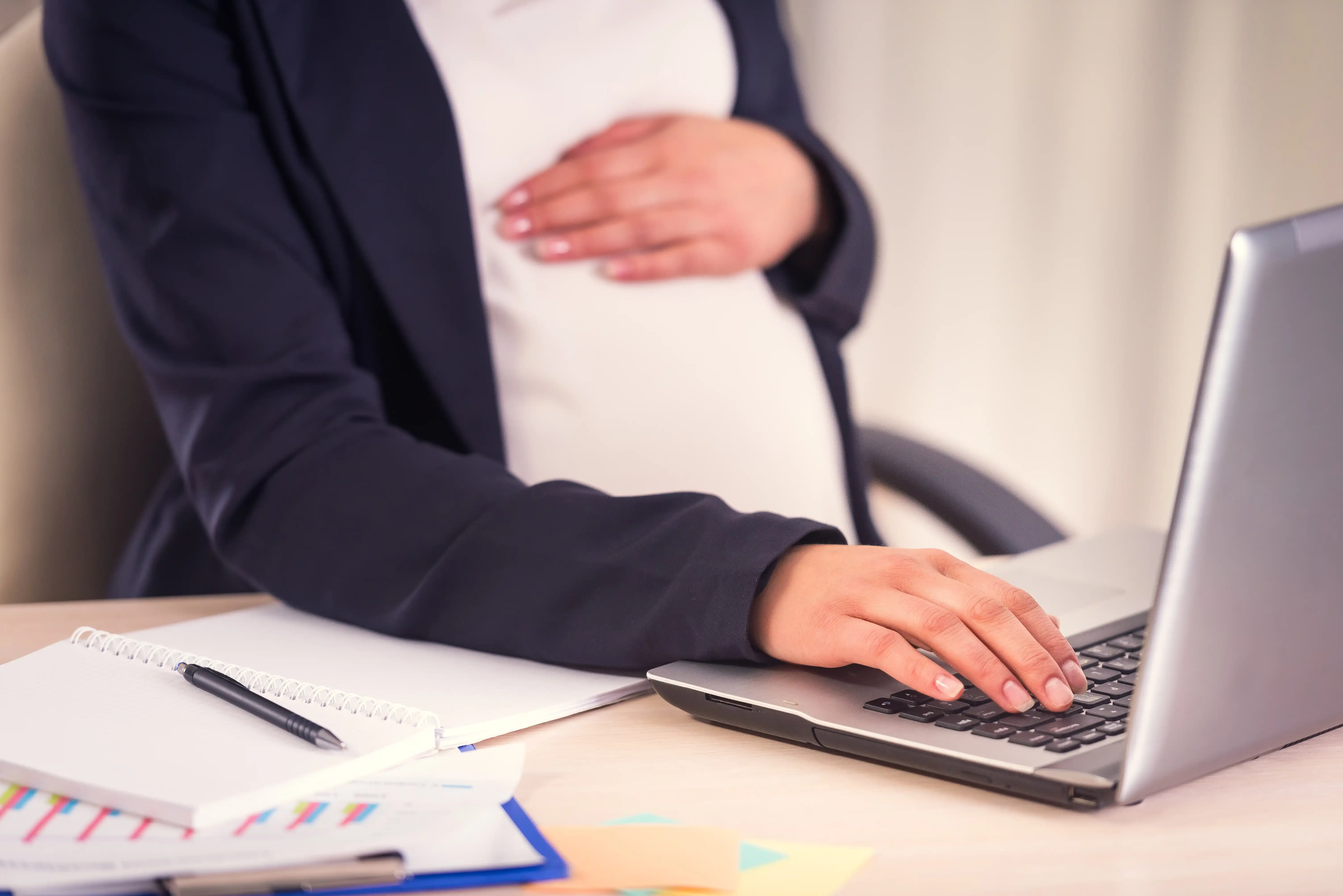 A pregnant employee wearing a blazer working on a laptop at her desk, illustrating job-protected leave rights under California's CFRA