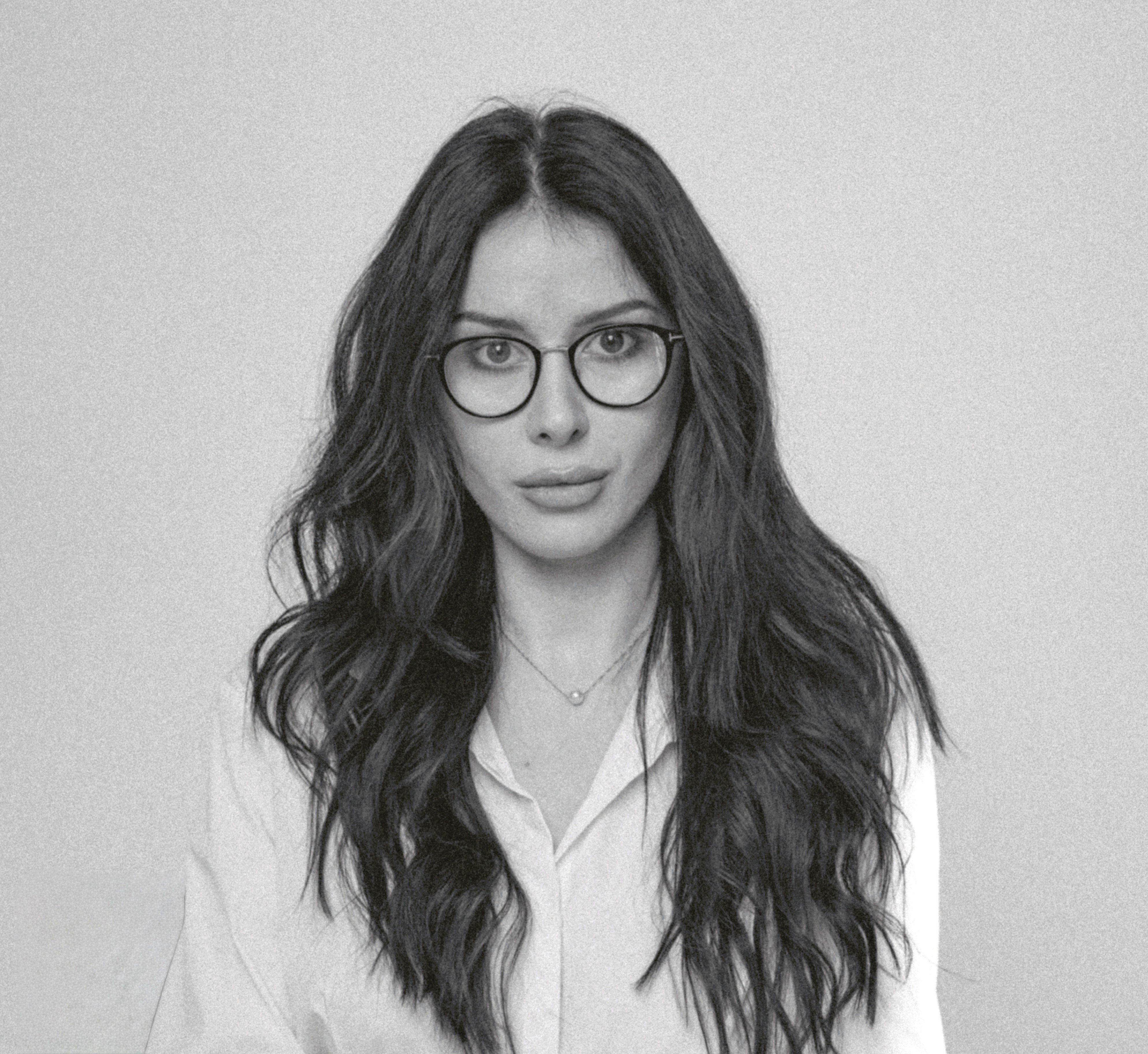 Professional headshot of a woman with brown hair in a white shirt against a neutral background.