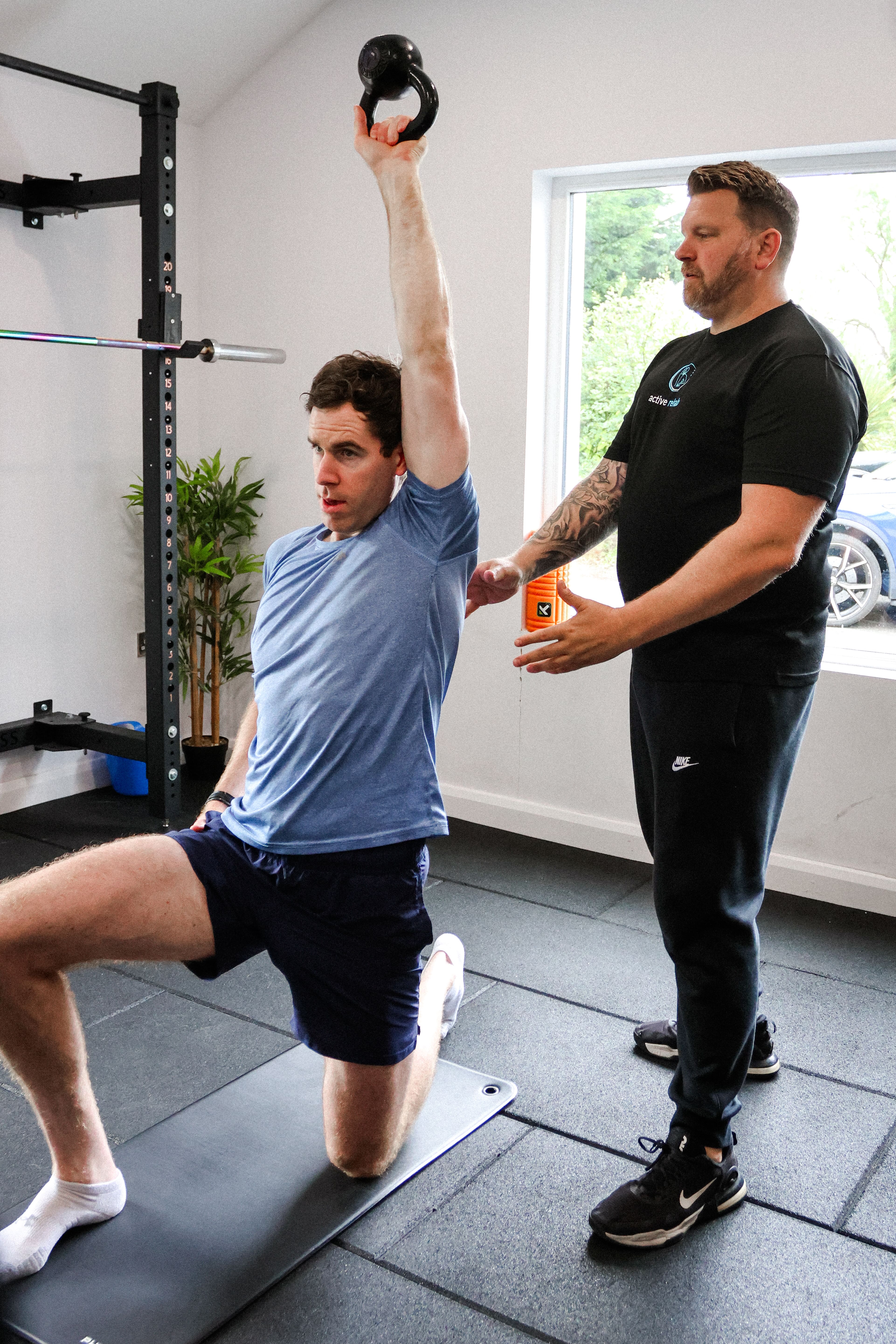 Therapist coaching a client through a controlled half-kneeling kettlebell press to build strength and shoulder stability.