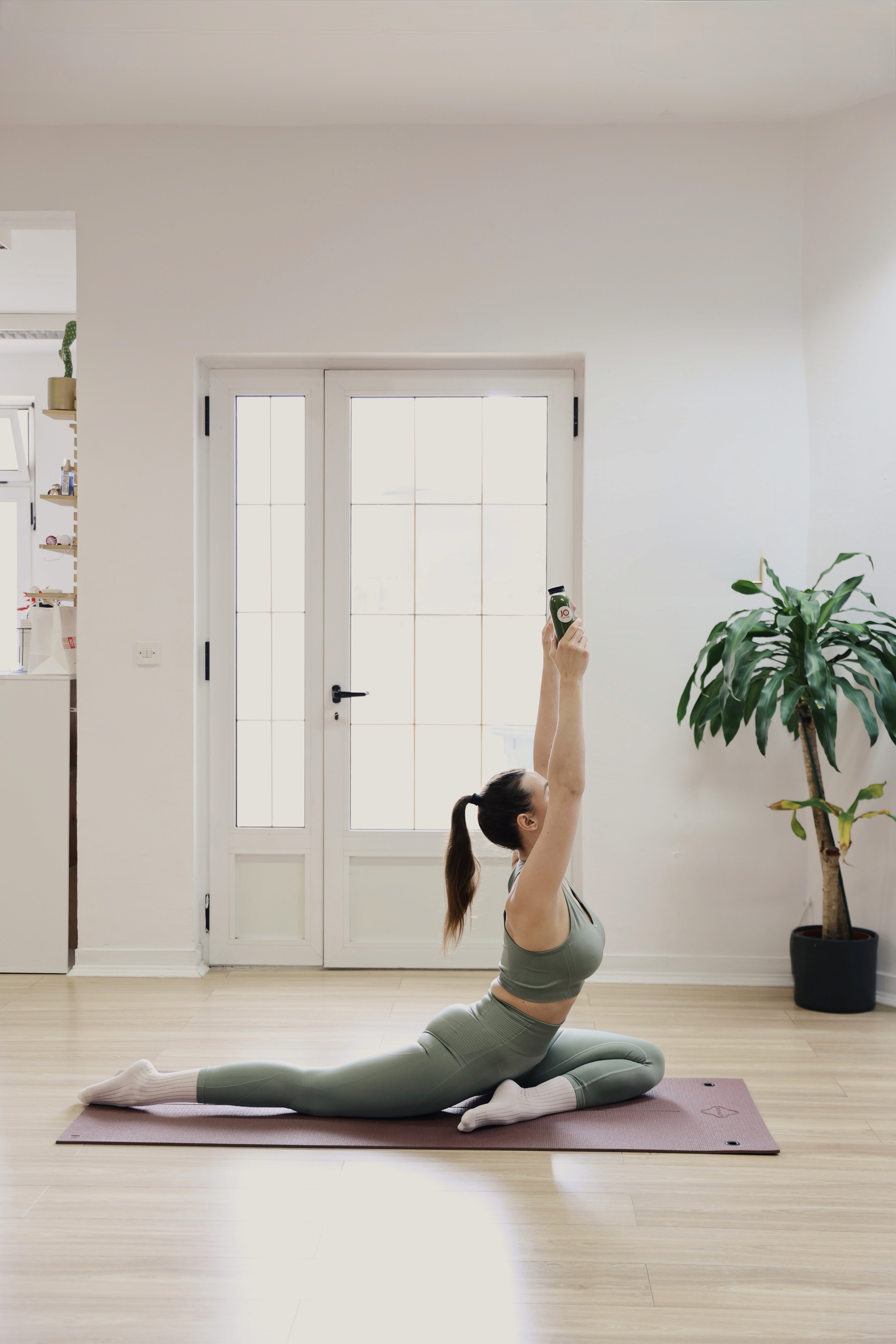 Woman performing a reformer Pilates stretch on a mat in a bright studio.