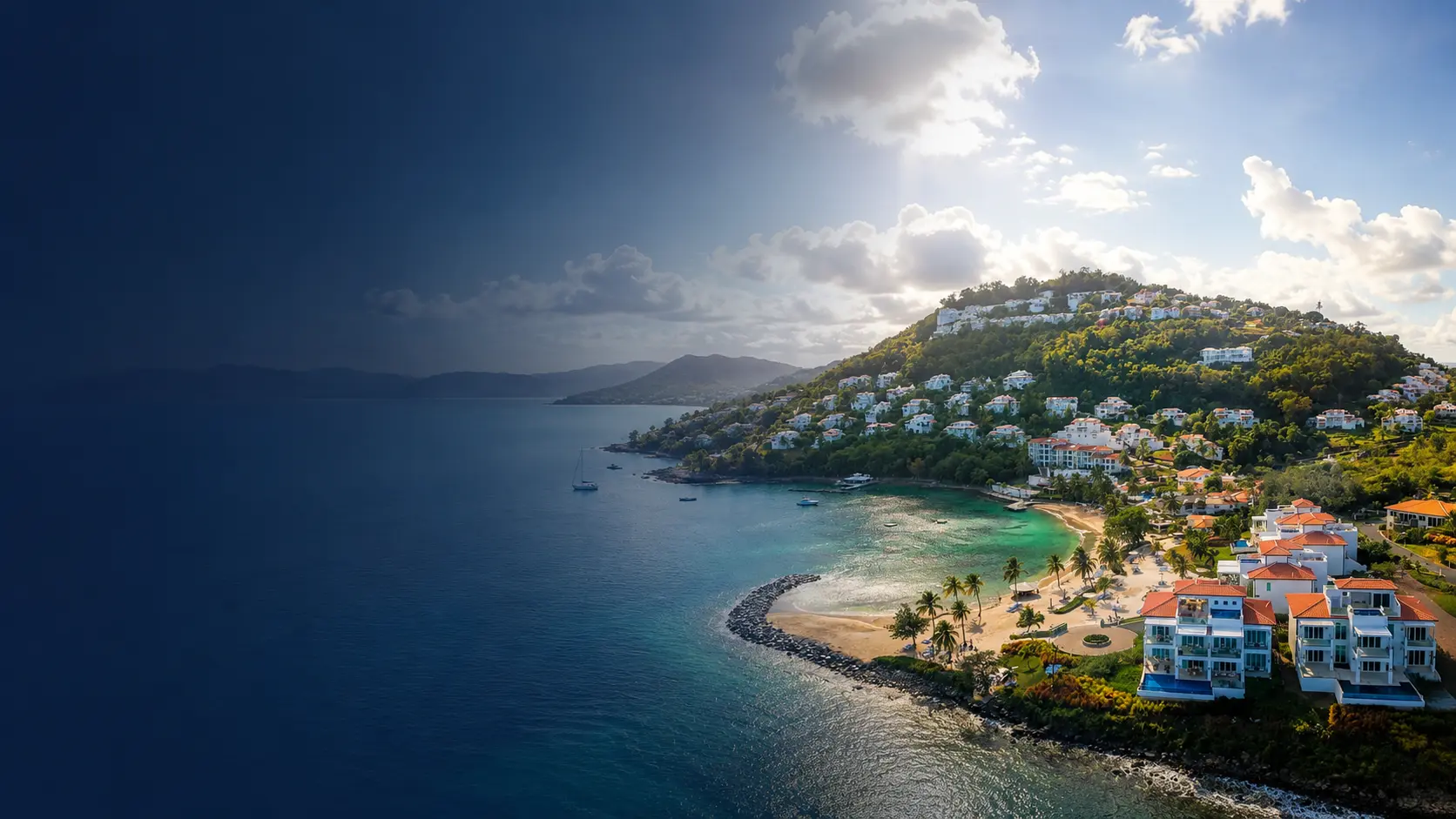 Aerial view of a hillside resort in Saint Lucia with red-roofed villas overlooking a turquoise bay and beach under a dramatic sky
