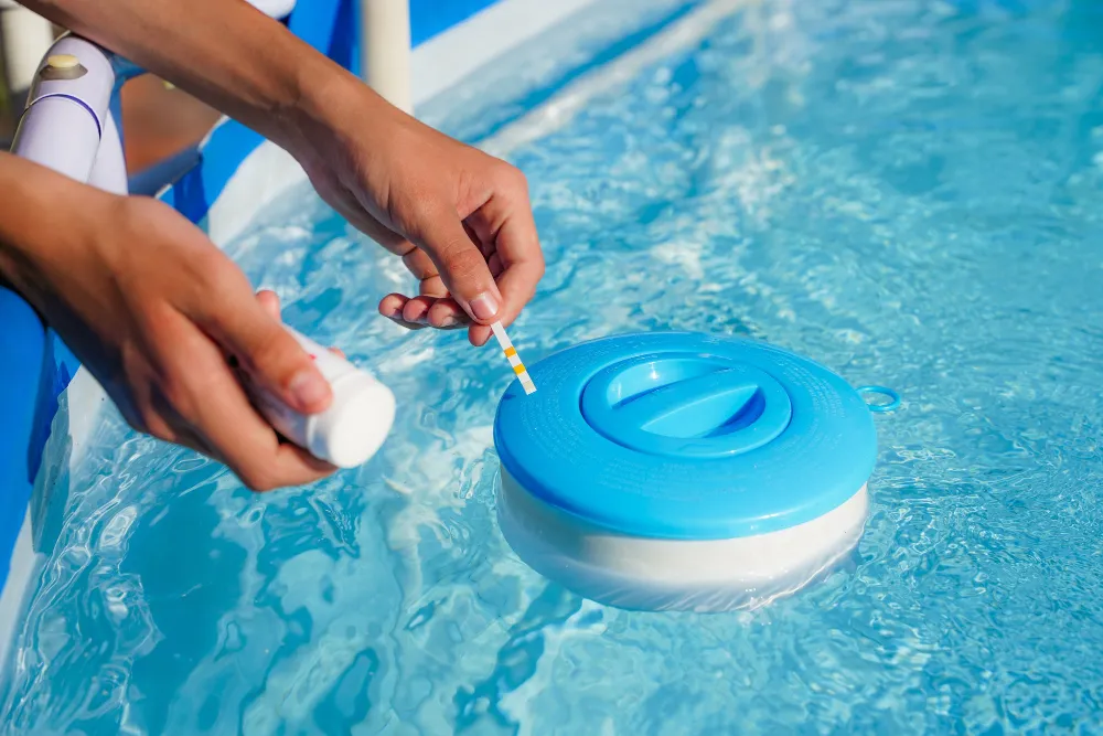 Close-up of a person using a test strip to check pool water near a floating chemical dispenser.