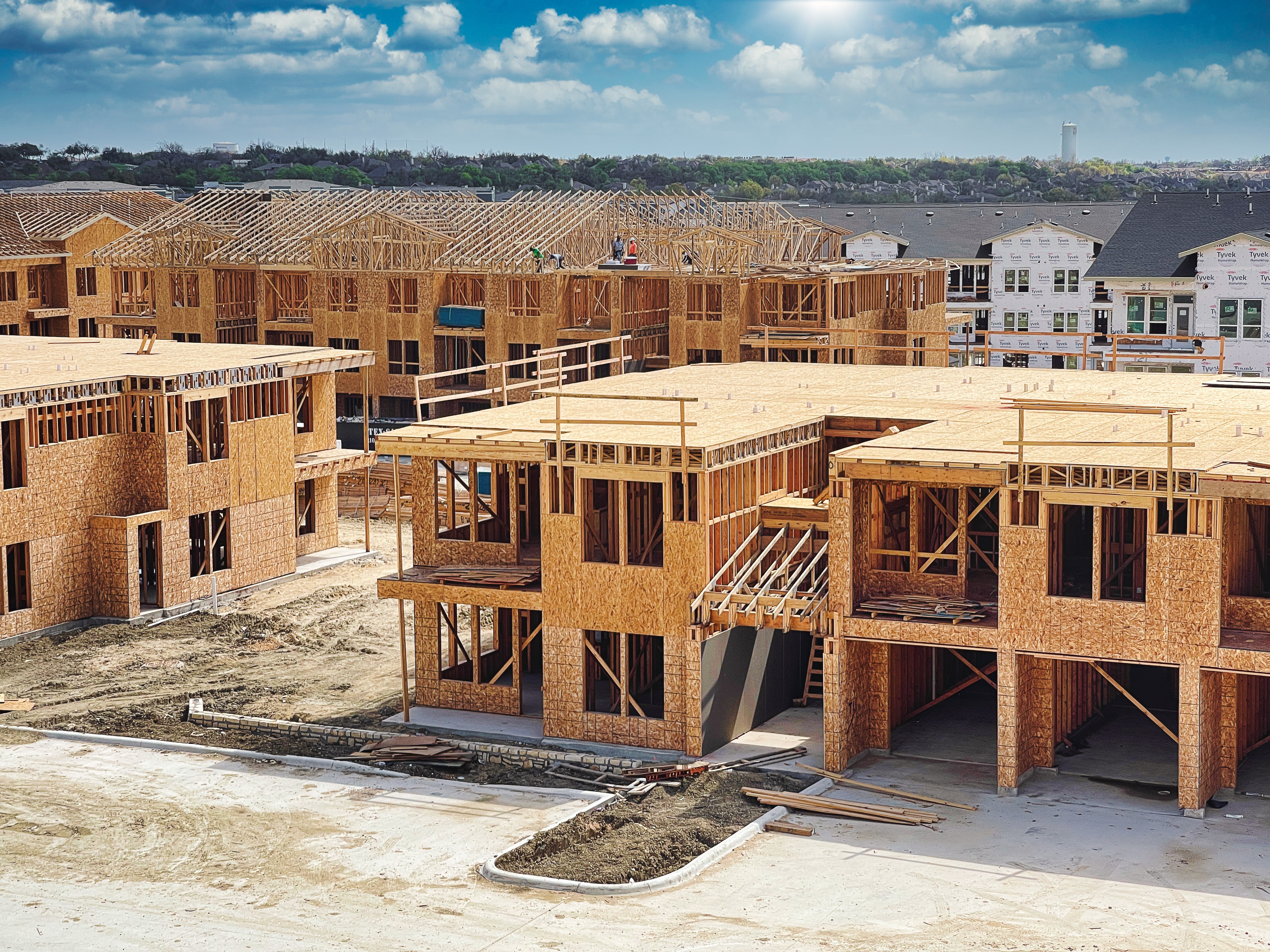 Aerial view of multiple wood-frame residential buildings under construction, showing exposed framing at various stages of completion