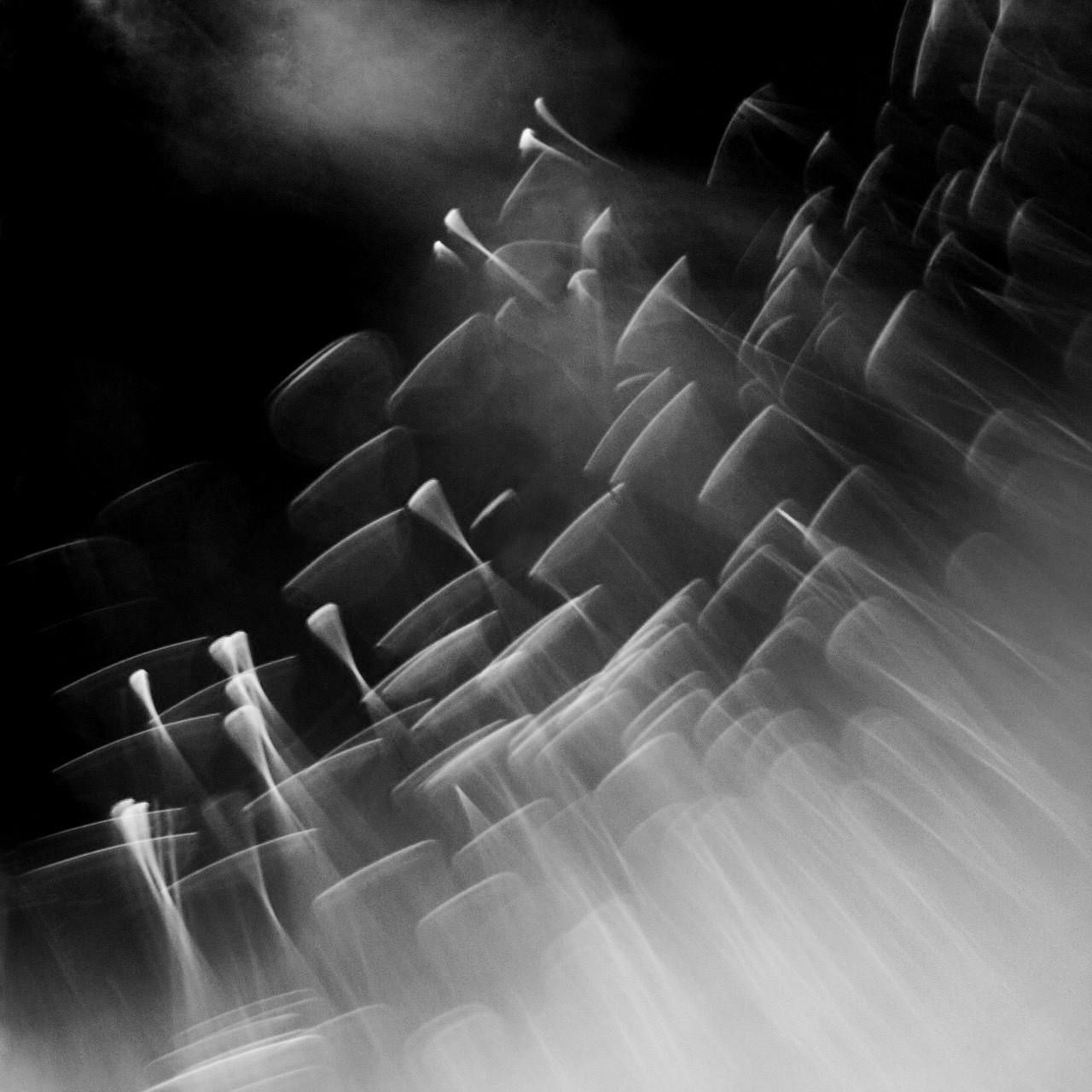 Abstract black and white photograph of dark forms and rising light streaks in motion, with a hazy atmospheric quality.