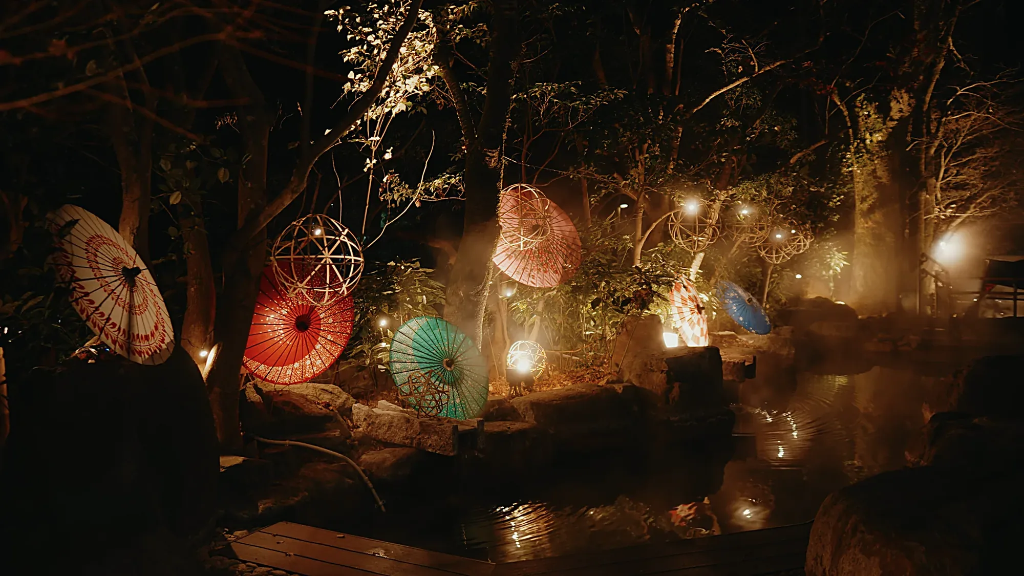 Lit paper parasols and lanterns set beside a steaming pool at Kurokawa Onsen