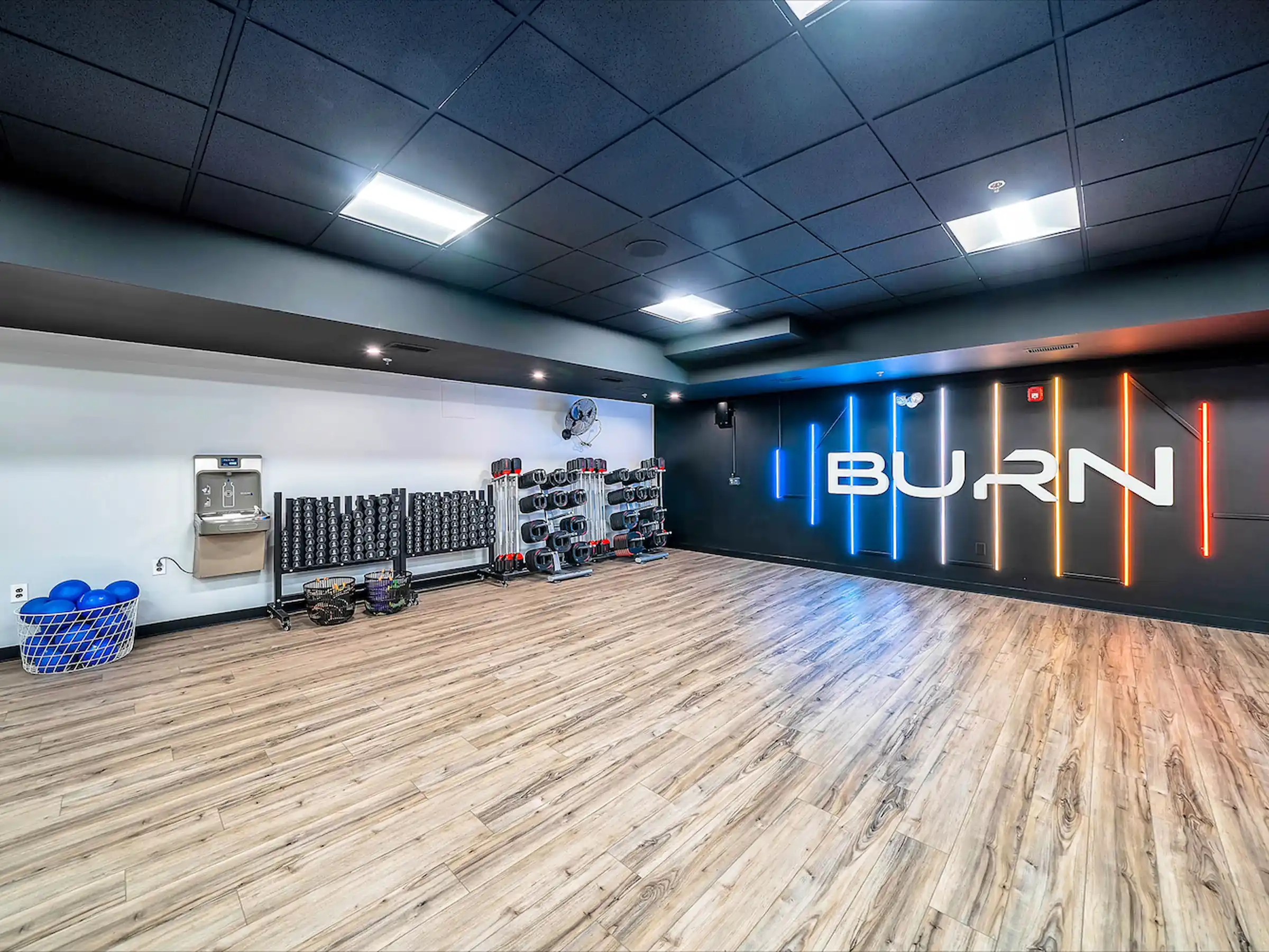 Luxury vinyl plank flooring in a boutique fitness studio with neon BURN signage, dumbbell racks, and water fountain.