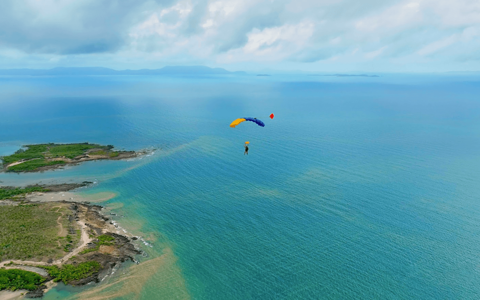 Skydiver descending over ocean near Airlie Beach with parachute.