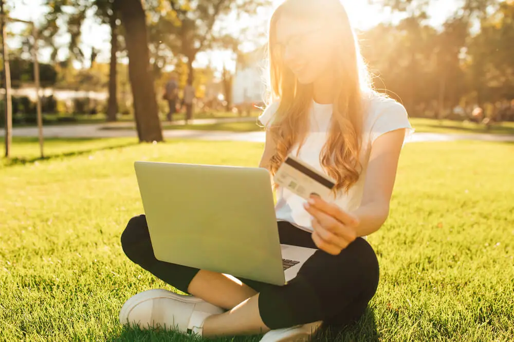 Woman shopping online with laptop and credit card in park