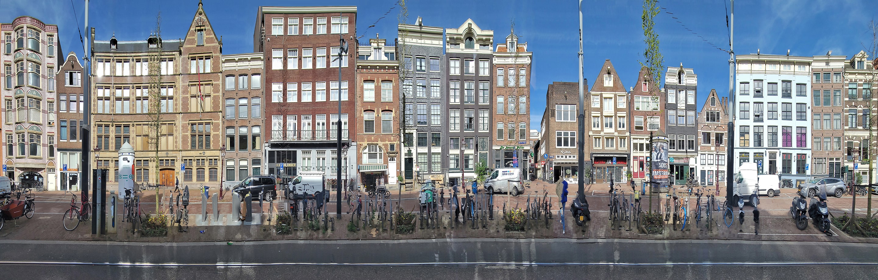 Panoramic photograph of canal-side buildings in Amsterdam, featuring a continuous row of narrow facades under a bright blue sky. Subtle distortions ripple through the architecture and reflections, blending realism with a sense of fluid motion.