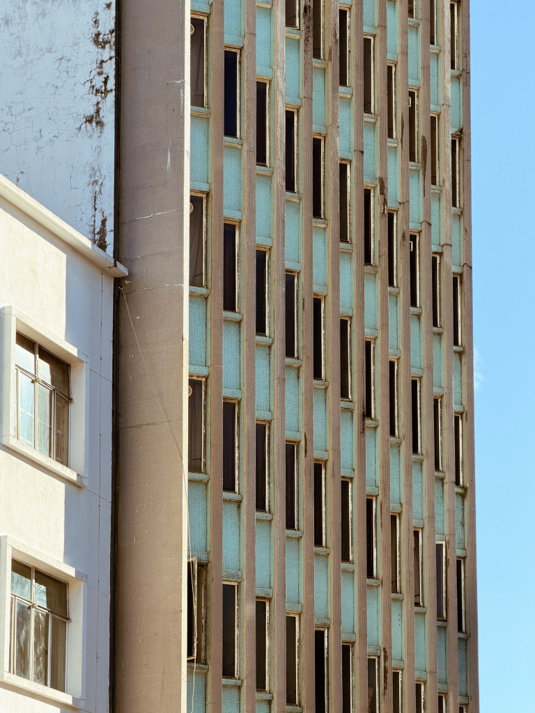 Close-up of an aging high-rise building with unevenly spaced windows and a weathered facade, adjacent to a white building.