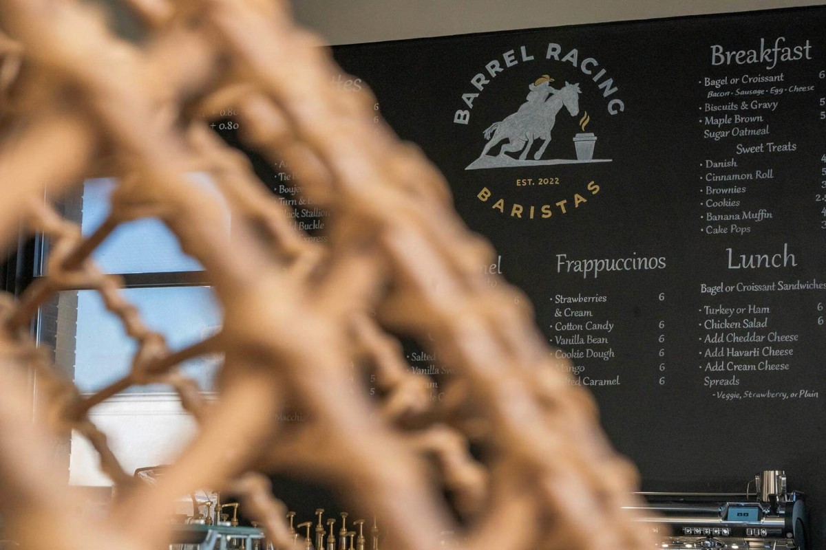 Four pieces of fried chicken or battered fish on a bed of salad greens, being heavily topped with shredded white cheese that is raining down onto the dish, set against a dark, rustic background of wood and pine cones.