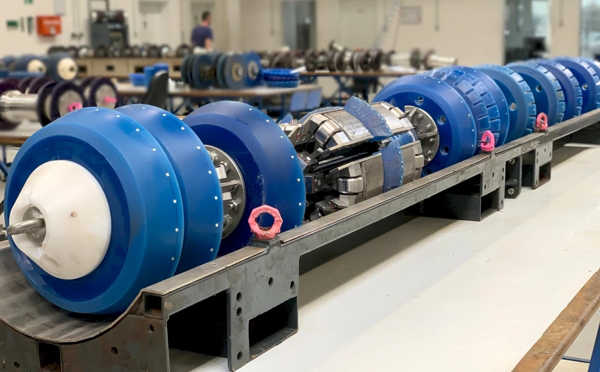 Nahaufnahme eines Rohrinspektionsgeräts, einer Reihe von blauen Rädern und metallischen Teilen, die auf einem Metallrahmen ausgerichtet sind und zur Wartung bereitstehen.