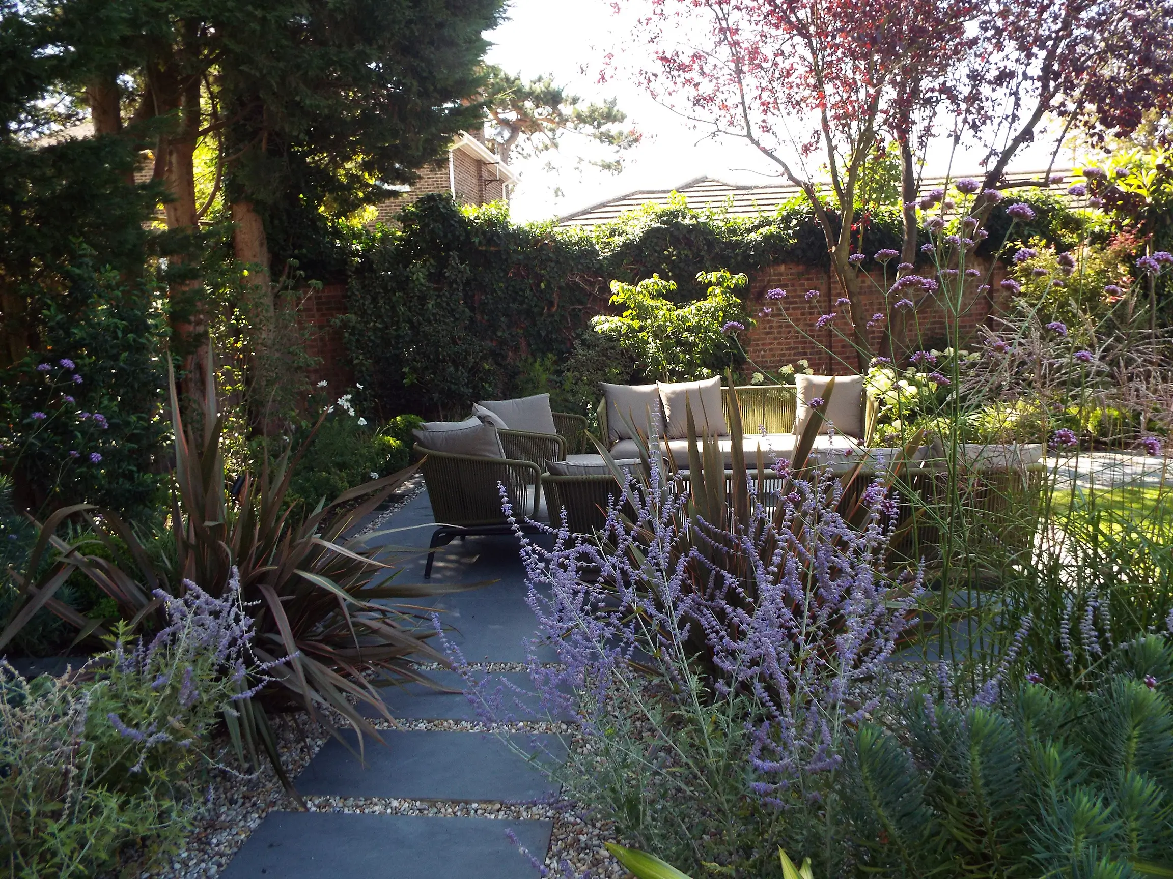A tranquil outdoor garden path surrounded by various plants and trees, bathed in natural sunlight.