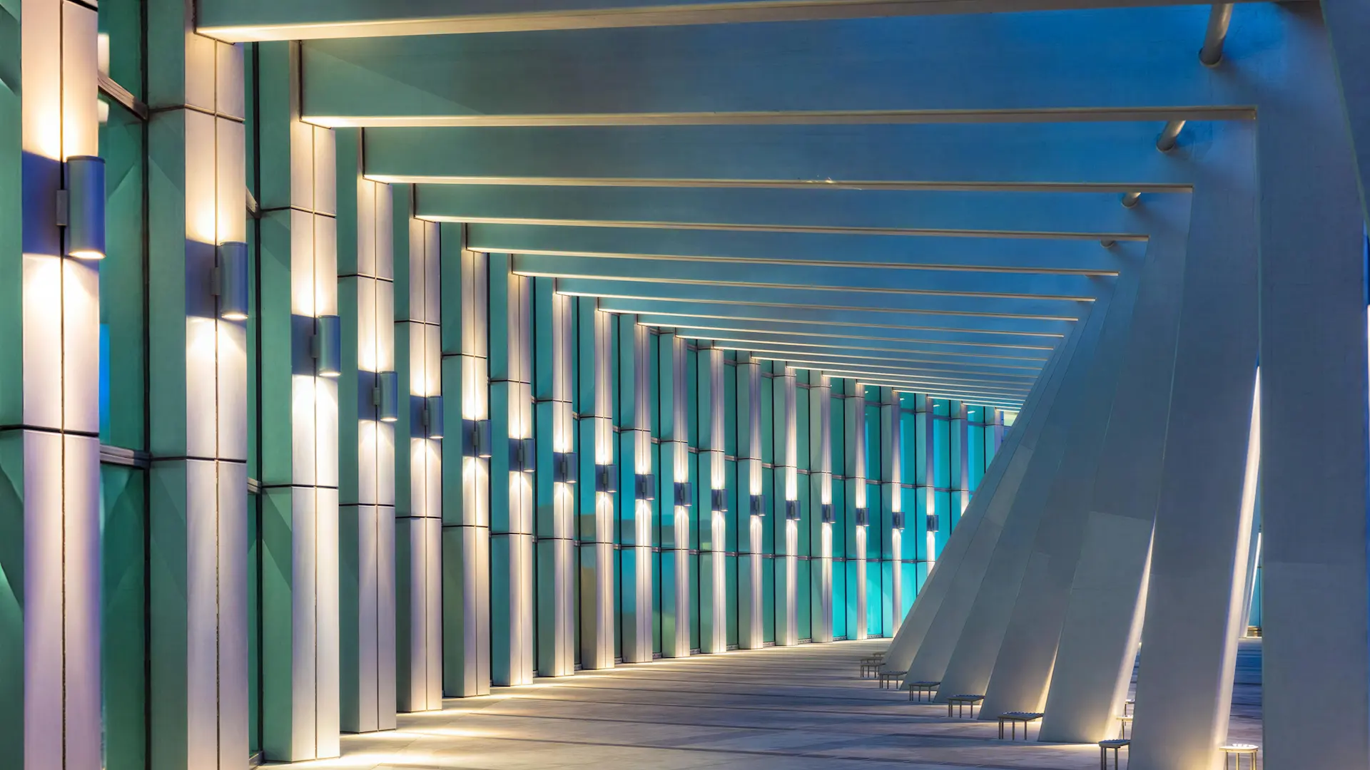 Modern corridor with exposed steel beams, structural columns, and illuminated vertical panels.