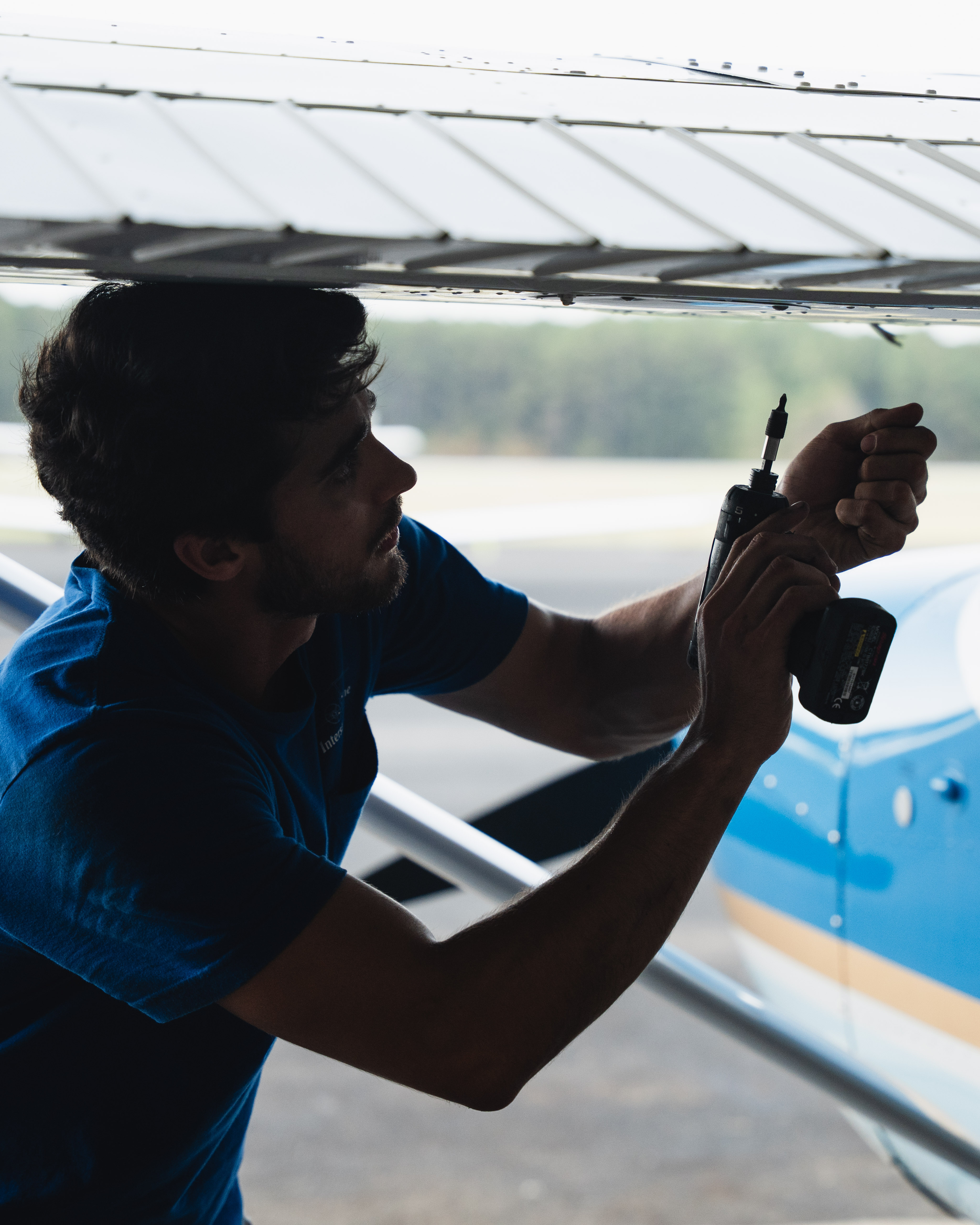 Hand holding a blue credit card over a white contactless payment reader on a wooden surface.
