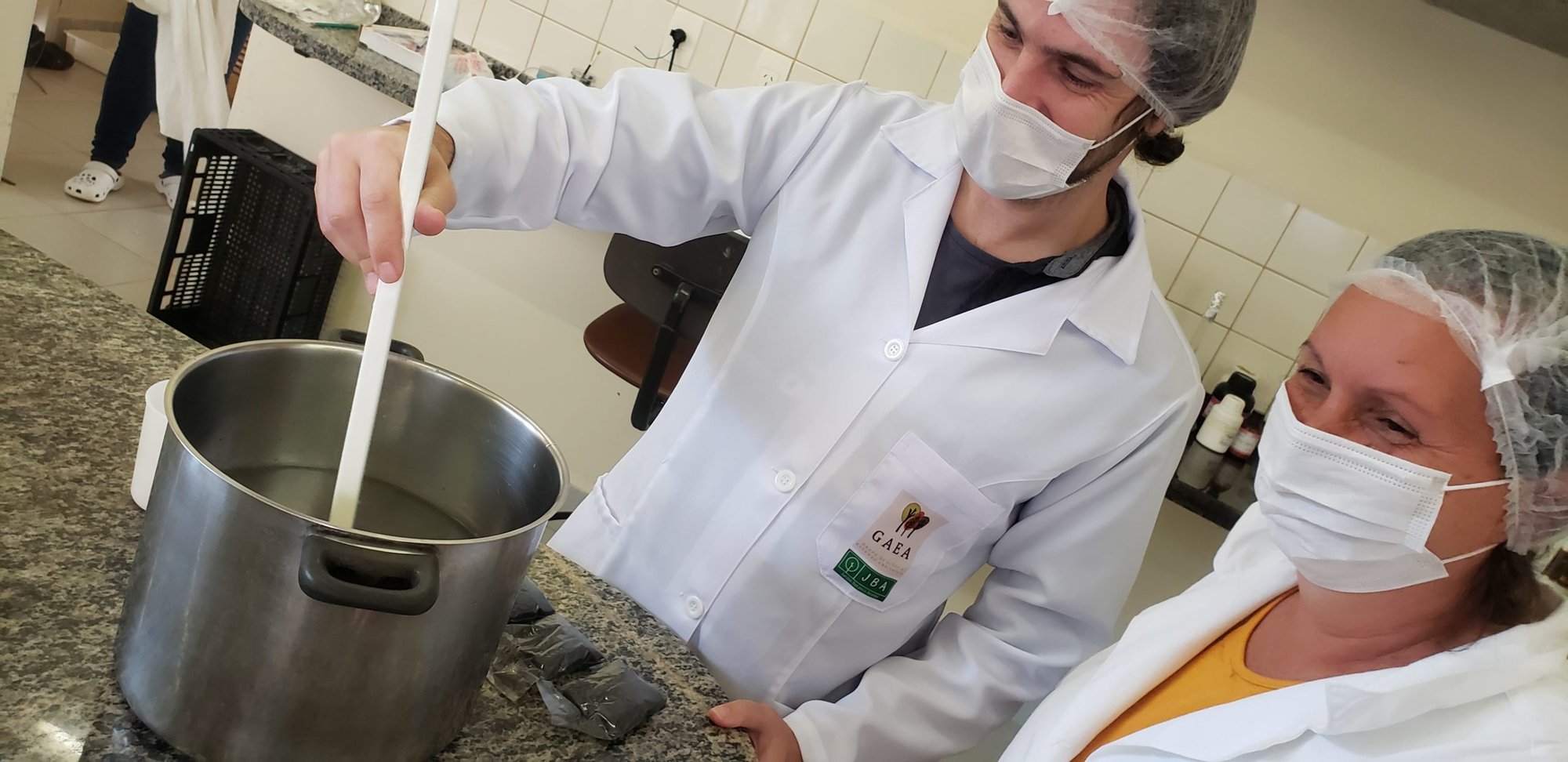 Participantes do curso de micropropagação, de touca e máscara, preparam meio de cultura em panela no laboratório