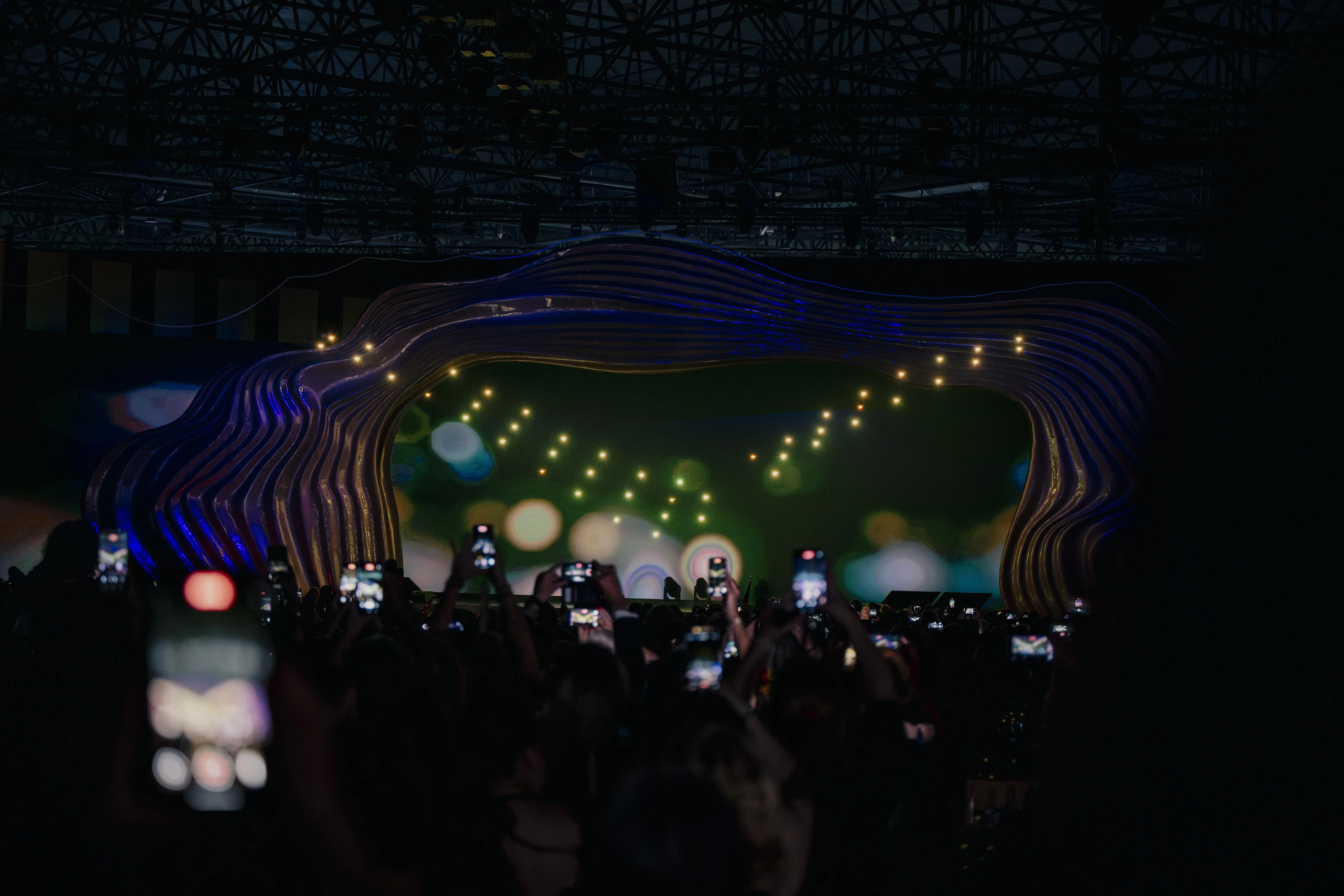 Audience filming the glowing wave stage with floating points of light during the show.