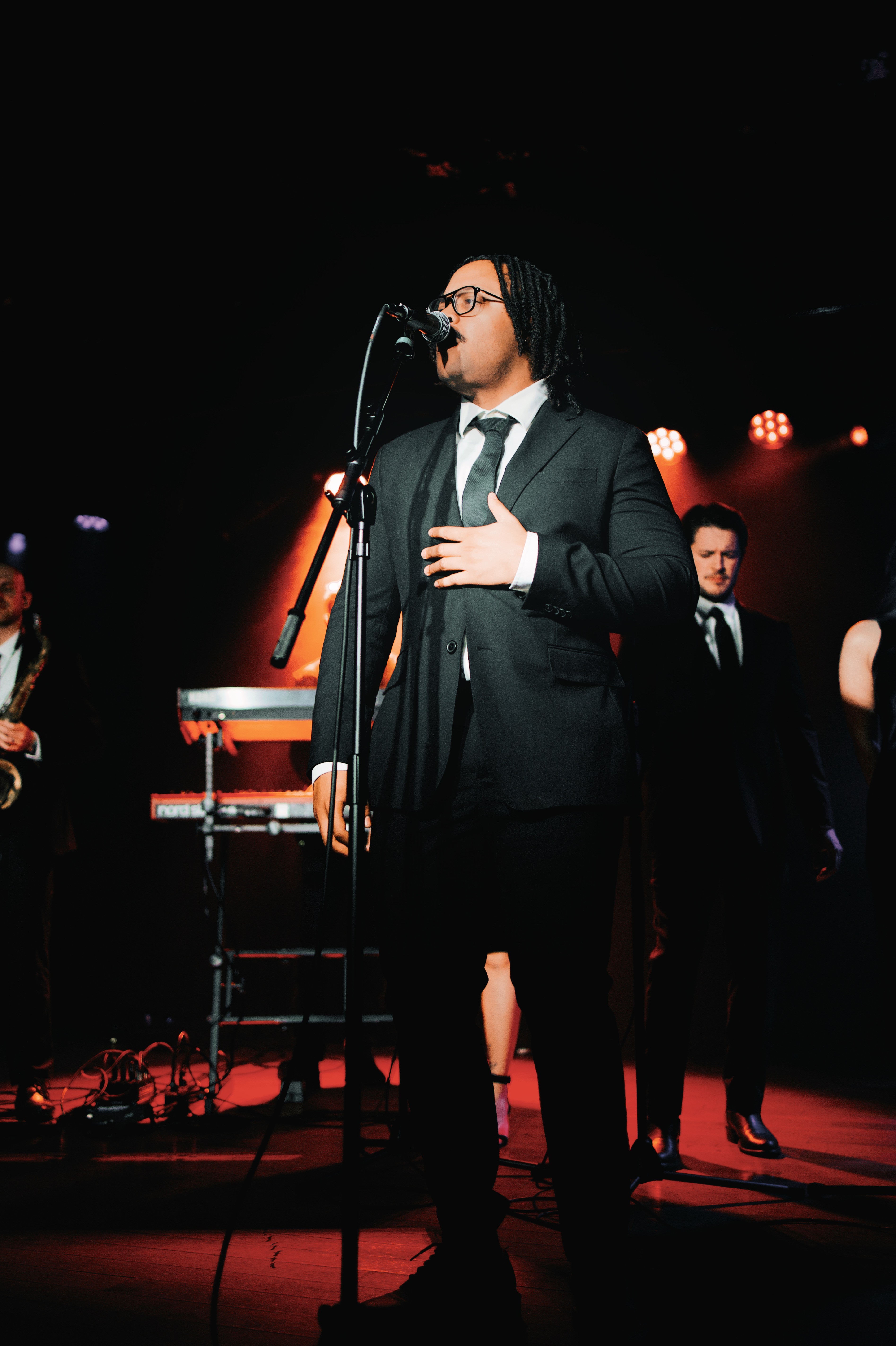 Three people in conversation with warm lighting, including a person wearing a hat and another person wrapped in what appears to be a textured shawl or sweater.