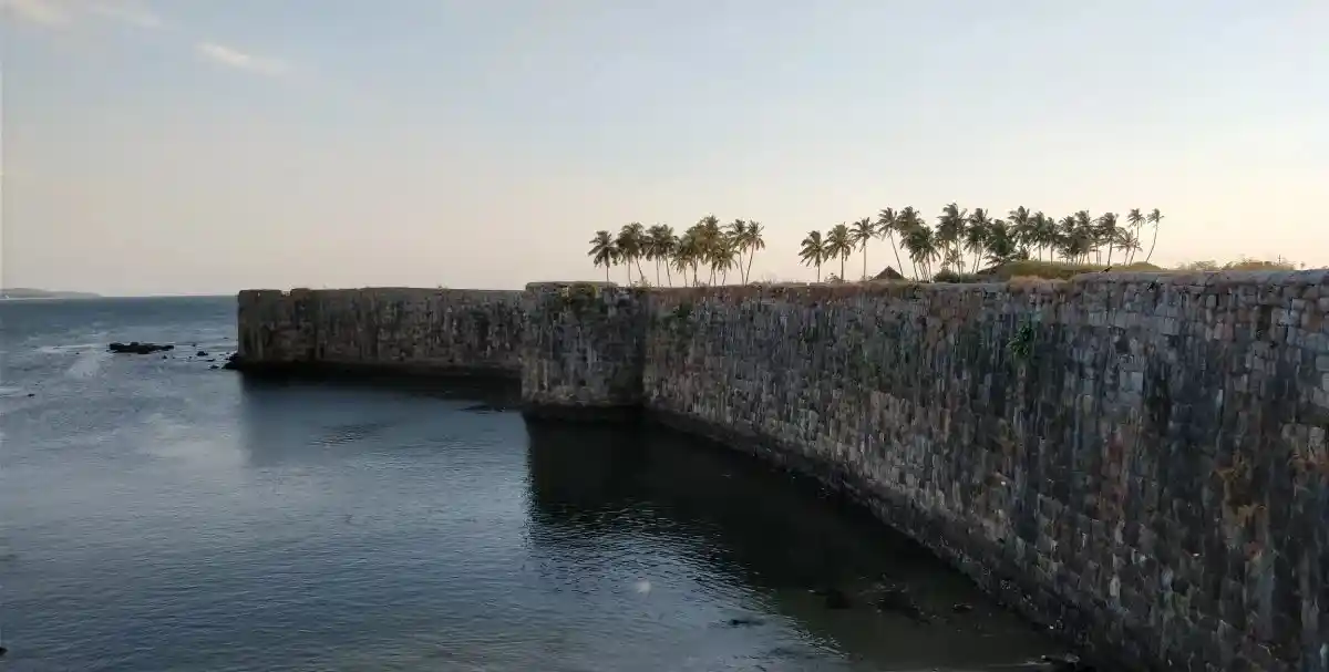 <img src="coastal-sindhudurg-goa.webp" alt="A stone fortress wall extends into the water at Sindhudurg, with a line of palm trees and a clear sky in the background.">