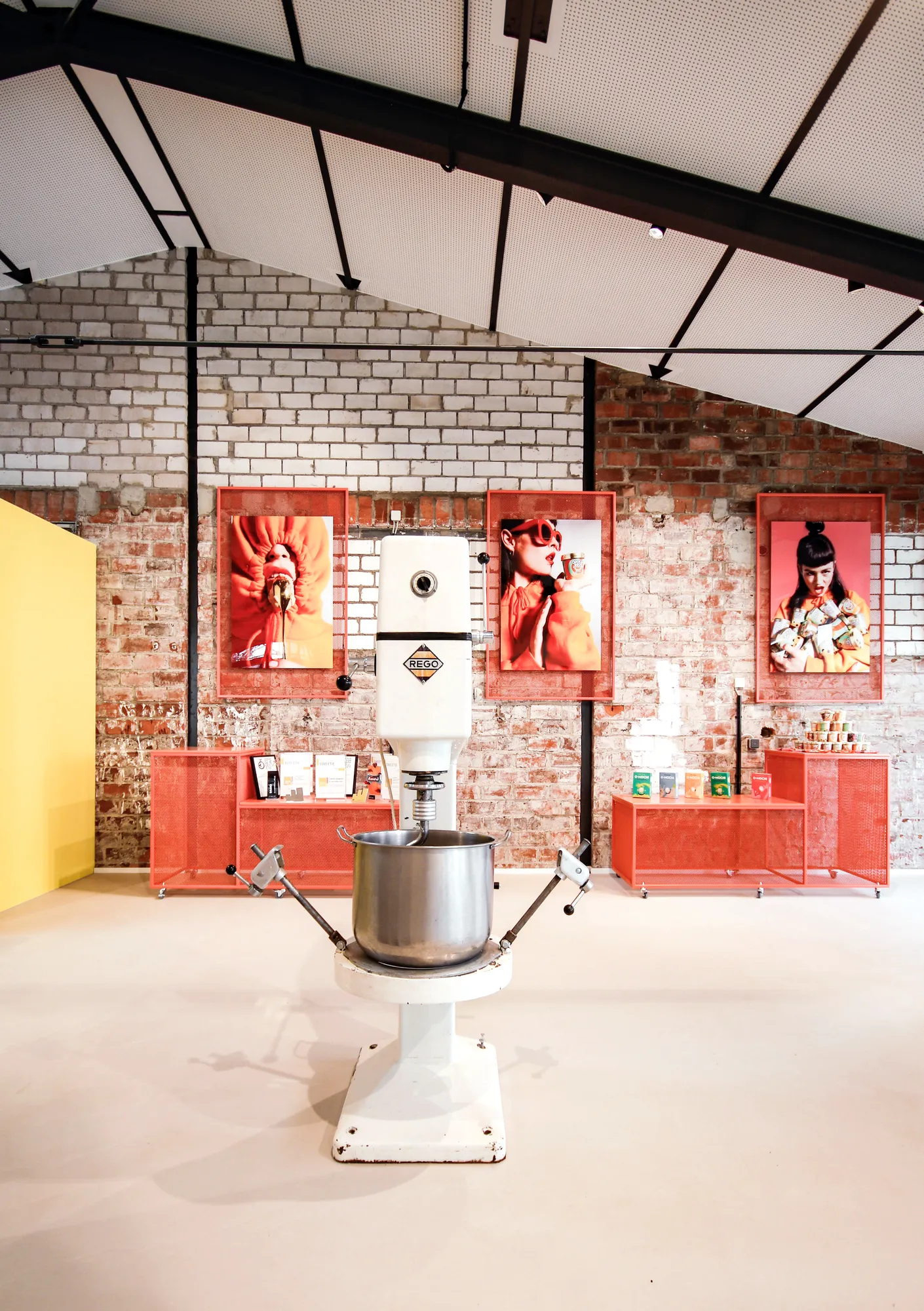 Vintage white industrial mixer in front of red display shelves with food portraits on the brick wall.