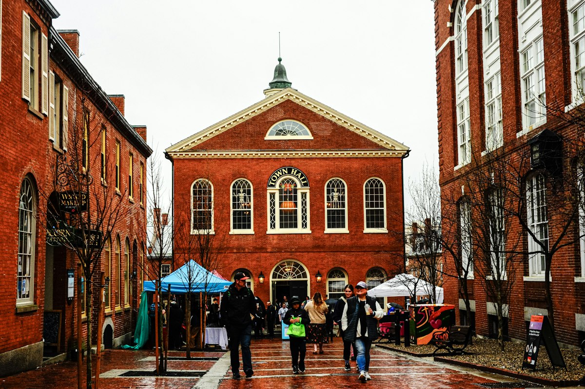 Visitors walking past a red brick civic building on a historic New England town street