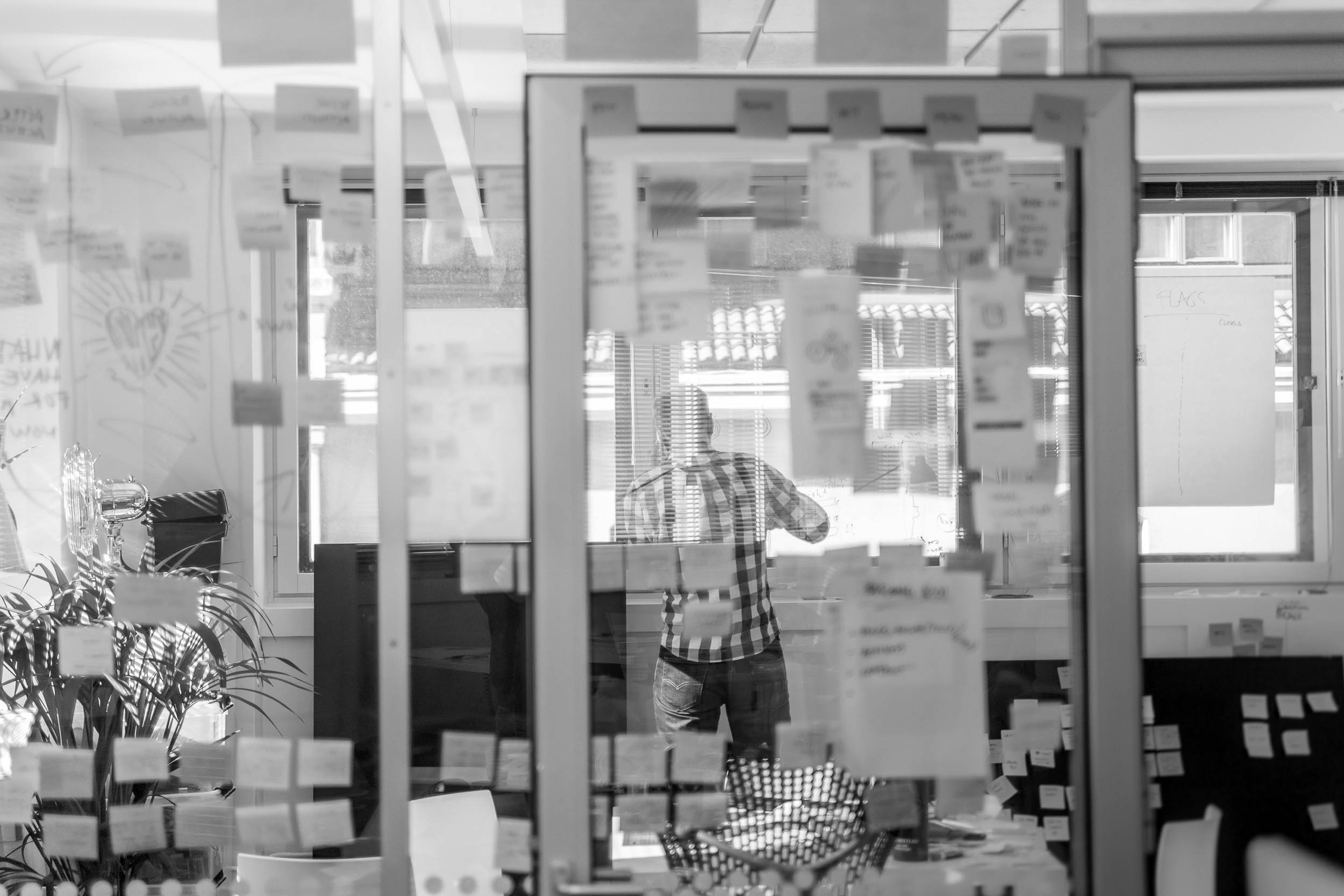 Black and white image of people working at a table with laptops, showing hands gesturing during discussion of digital content displayed on screens, with fabrica® logo in the corner.
