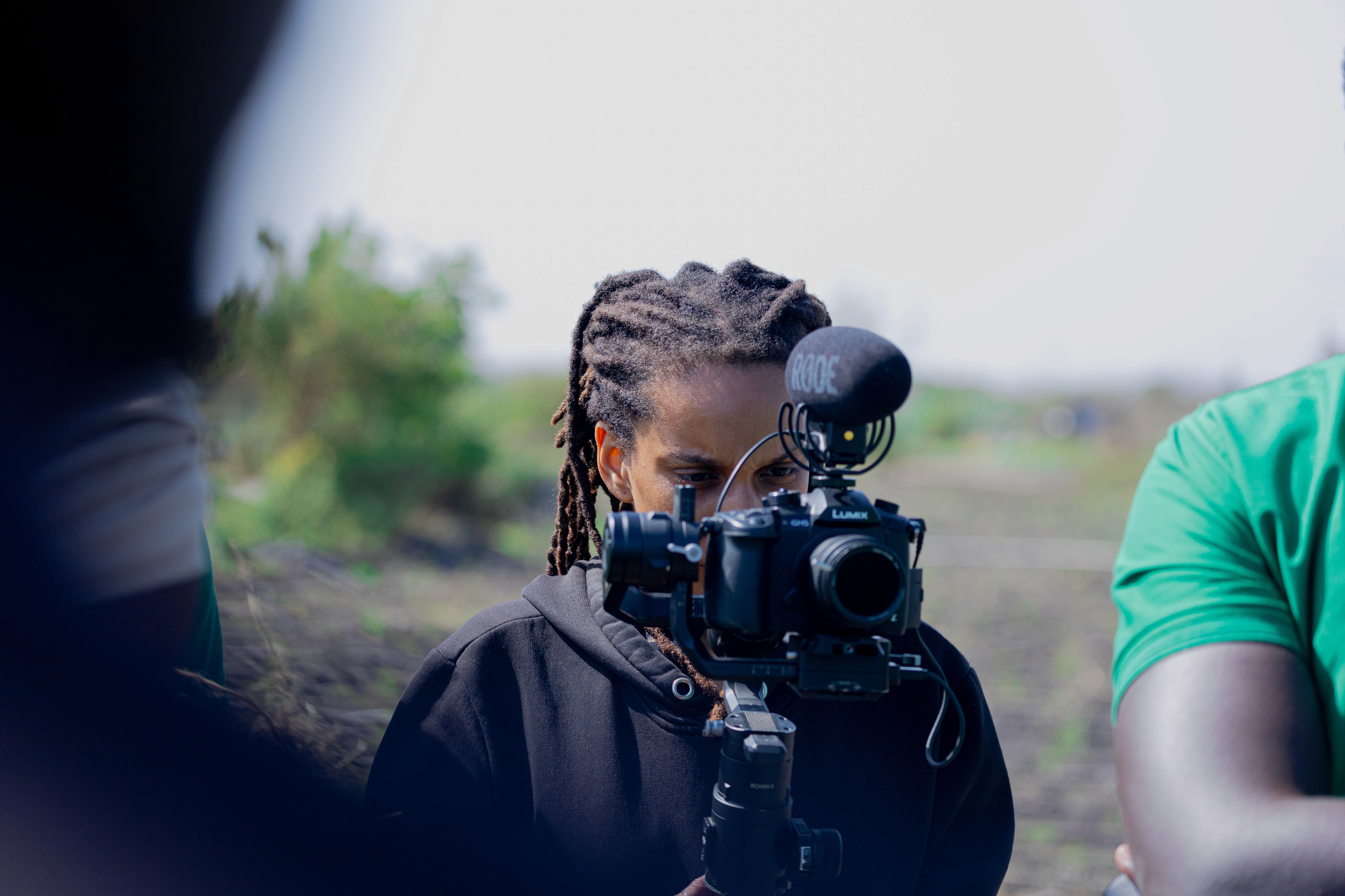 A woman with curly red hair, wearing a white top, lace skirt, and brown boots, walks while carrying a large bouquet of sunflowers over her shoulder.