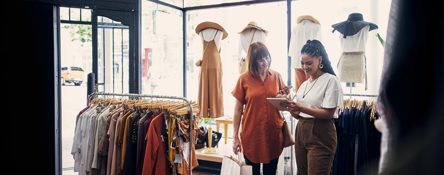 Two women shop for clothes with the help of a tablet.