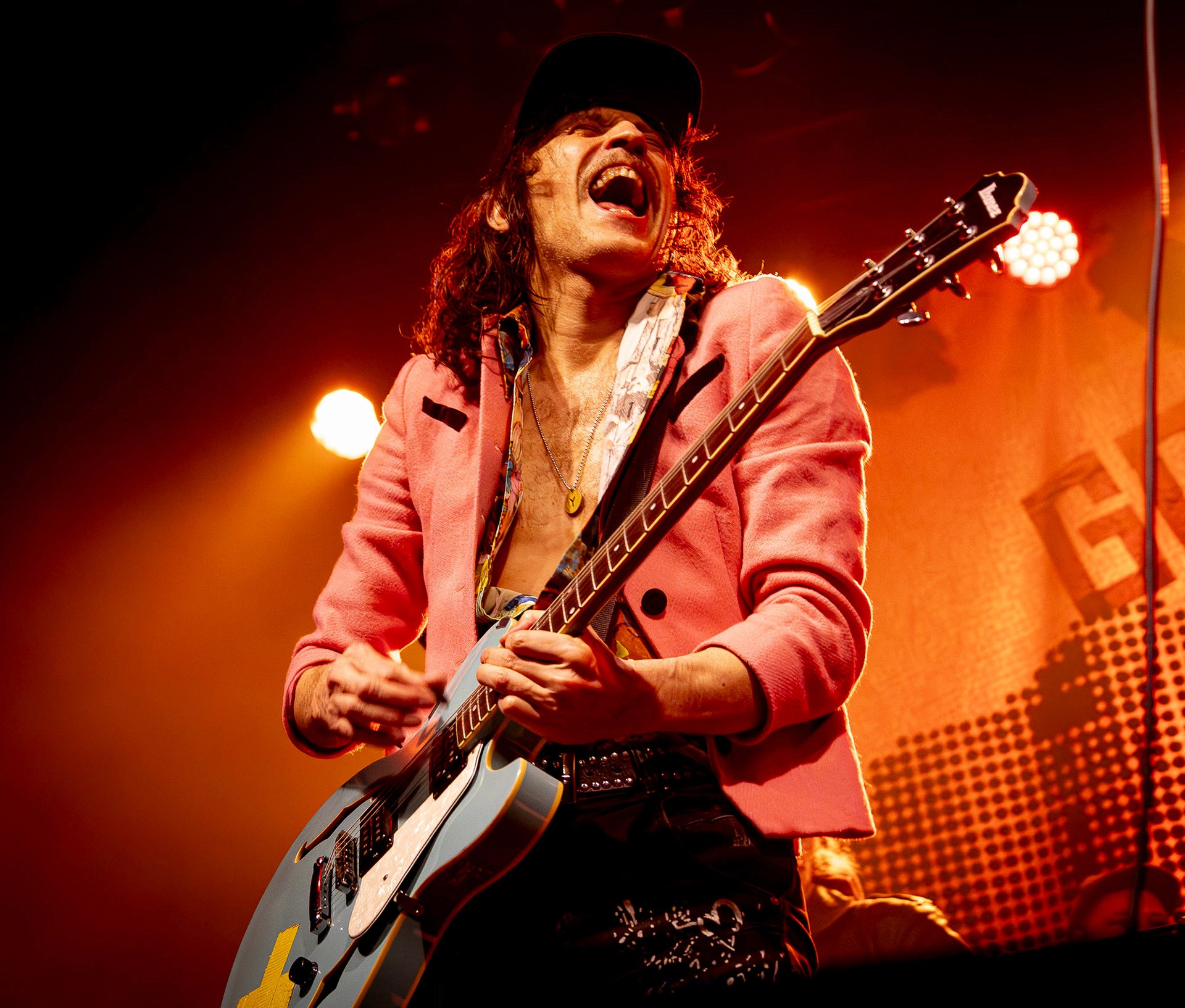 High-energy live concert photo capturing a musician leaping high mid-air on stage during a performance, illuminated by intense purple spotlights and stage haze.