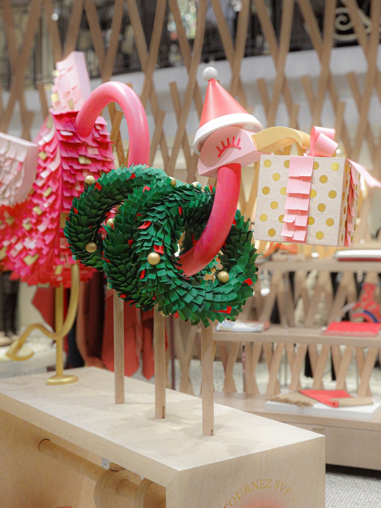 Close-up of a whimsical animated wooden ostrich toy for the Hermès holiday scenography, featuring a pink neck, a Christmas hat, and holding a gold-dotted gift box, designed by WM Paris.