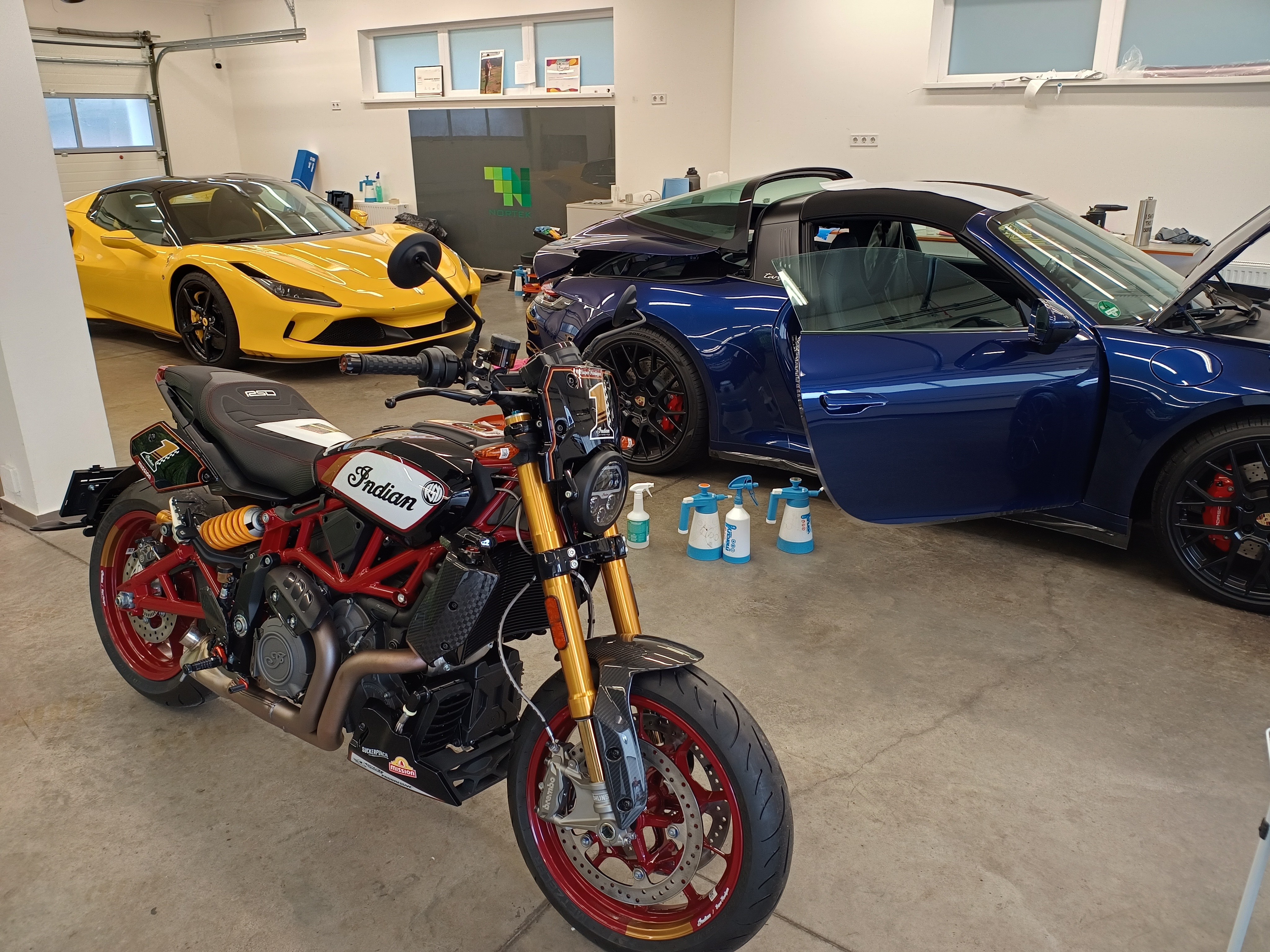 Prémium járművek védelme a Norteknél: egy egyedi Indian motorkerékpár, egy sárga Ferrari 458 és egy kék Porsche 992 Targa karosszériavédő fóliázáson.