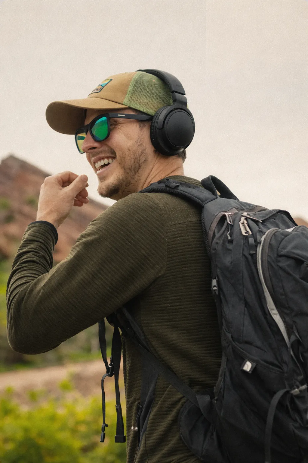 Neura Health Smiling man wearing a cap and over-ear headphones with a backpack outdoors.