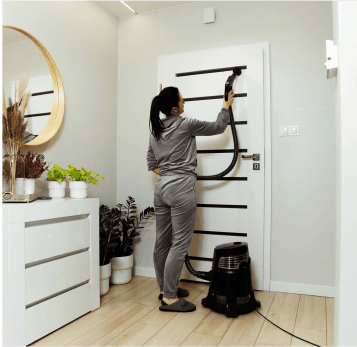 Woman cleaning a black metal shelf with a vacuum cleaner in a modern room.