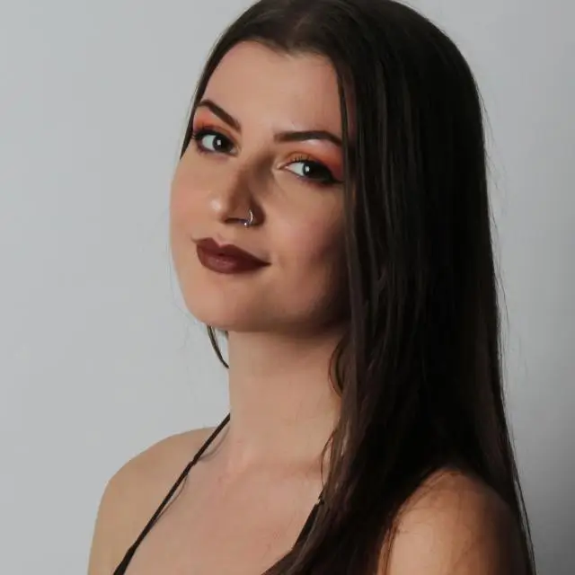 A woman with long dark hair and a neutral expression poses against a light background, wearing subtle makeup.
