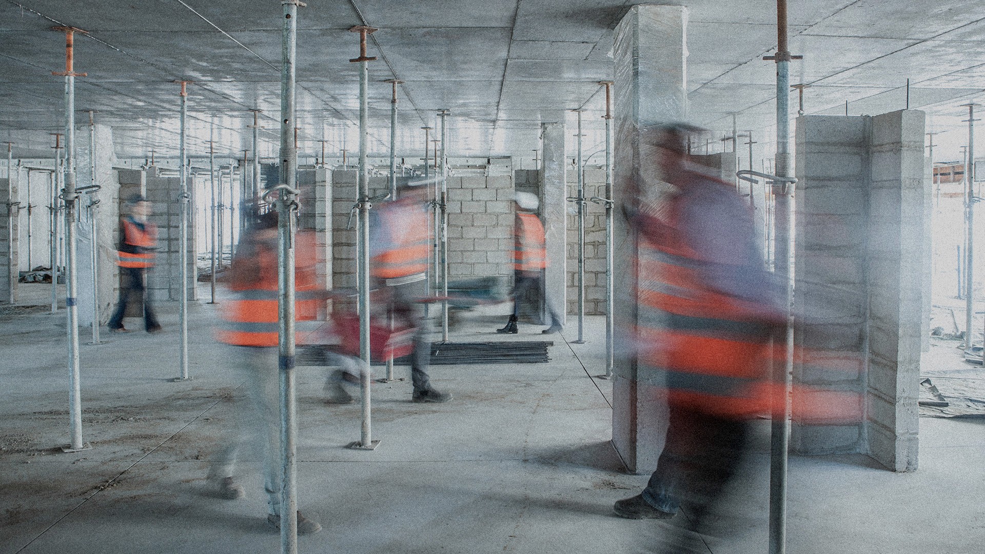 A grainy motion blur picture of construction workers in orange vests walking in a construction site.
