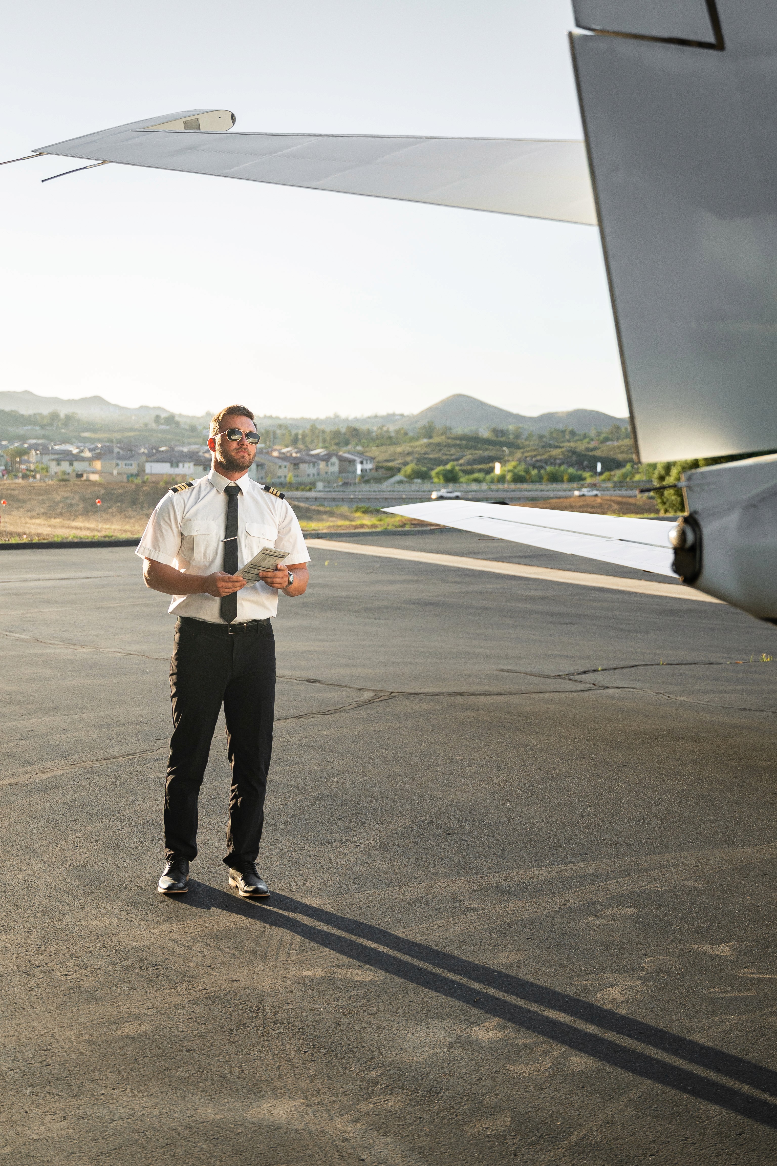 Man wearing an olive green jacket and black shirt, sitting and smiling in front of a light wooden background.