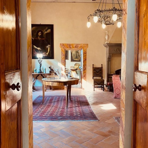 一个温暖的房间，房内设有铺着红色地毯的木制餐桌、吊灯、画作、壁炉，以及各种椅子和装饰品。