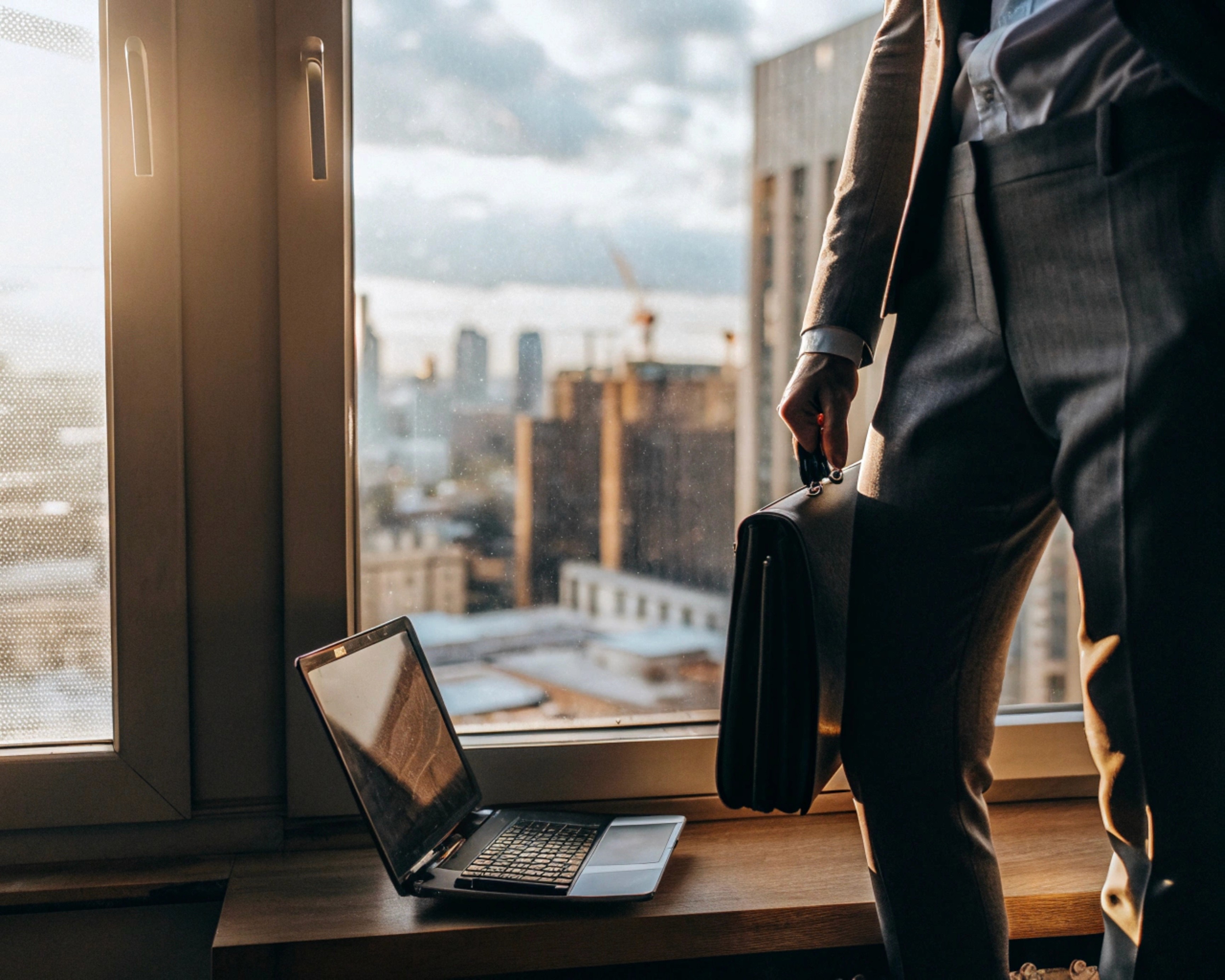 Person relaxing with feet up on a desk with a laptop, phone, and sunlight streaming through a window.