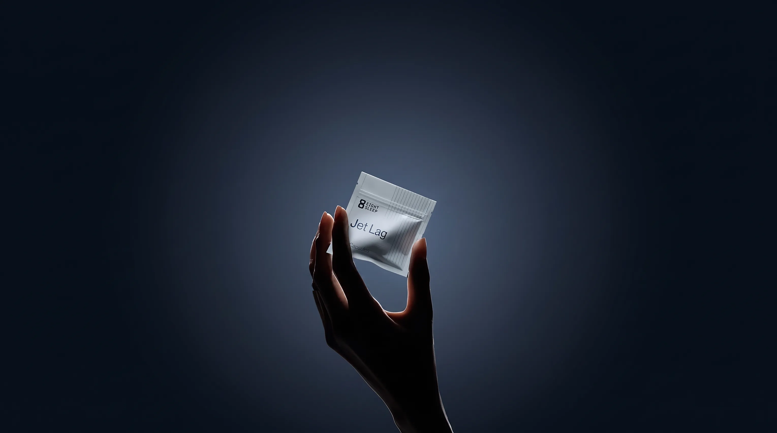 Hand holding an Eight Sleep Jet Lag supplement sachet against a dark blue background