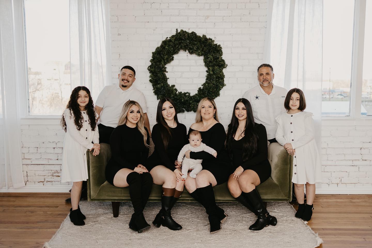 Large family of 9 all sitting on a large couch with the woman in front holding a baby.